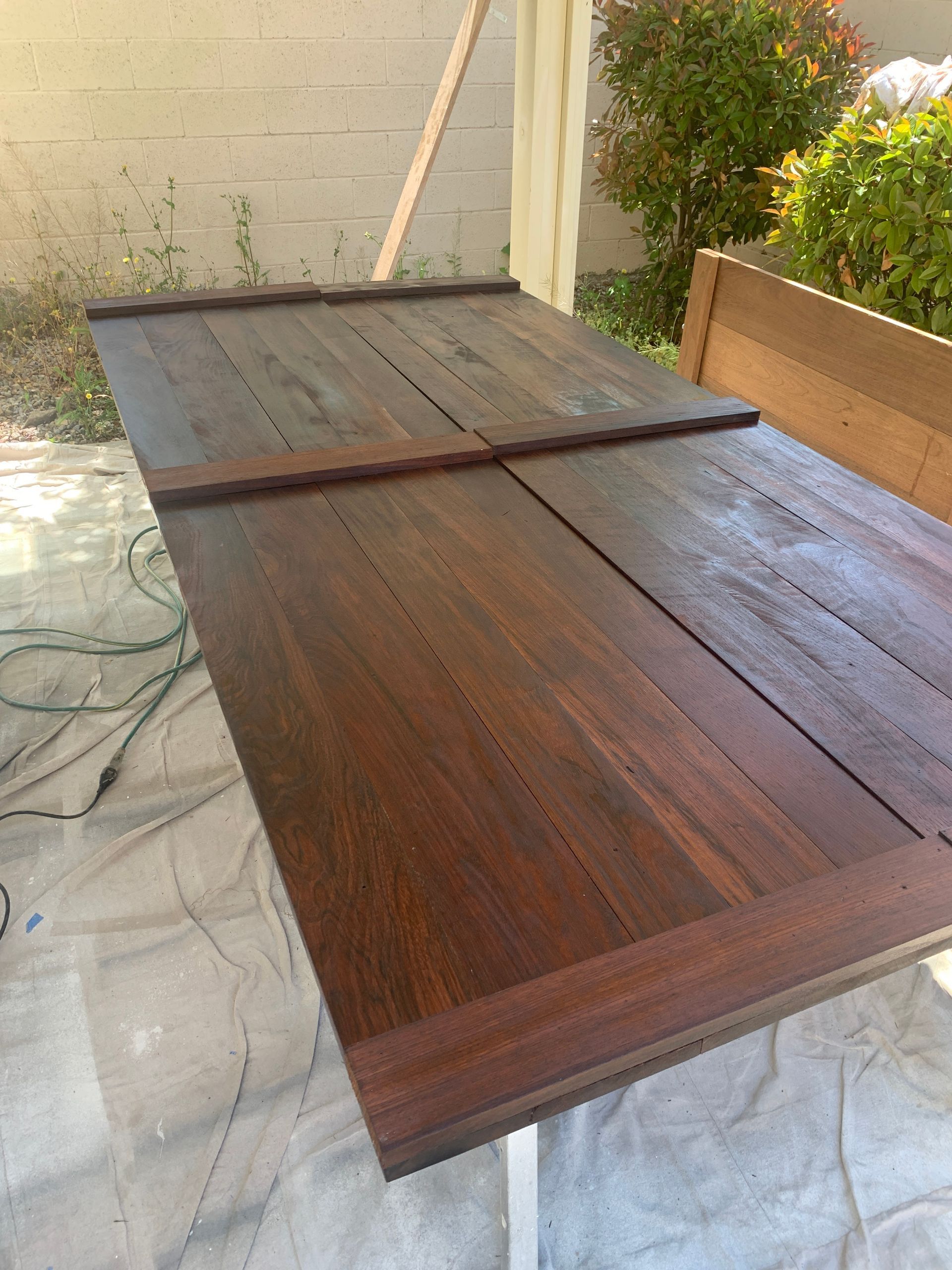 Wooden deck panels laid on a patio, with one dark brown section open and others gray and weathered.
