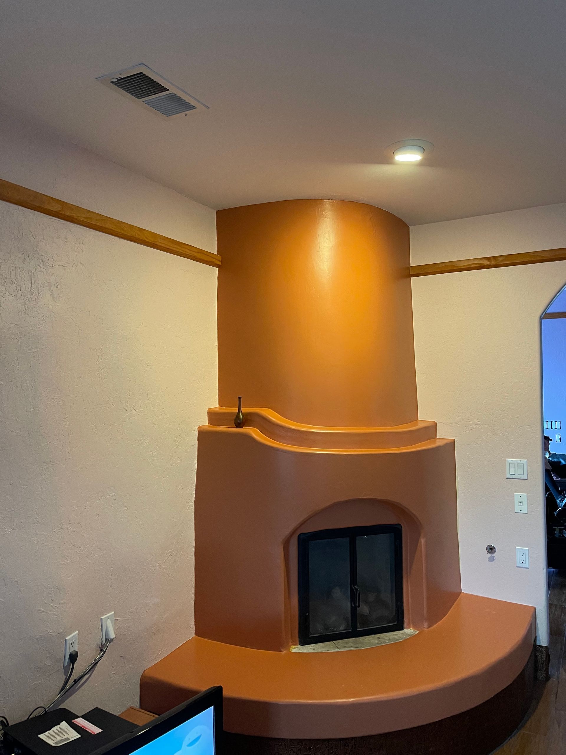 Living room fireplace with orange curved chimney and black firebox, centered against beige walls