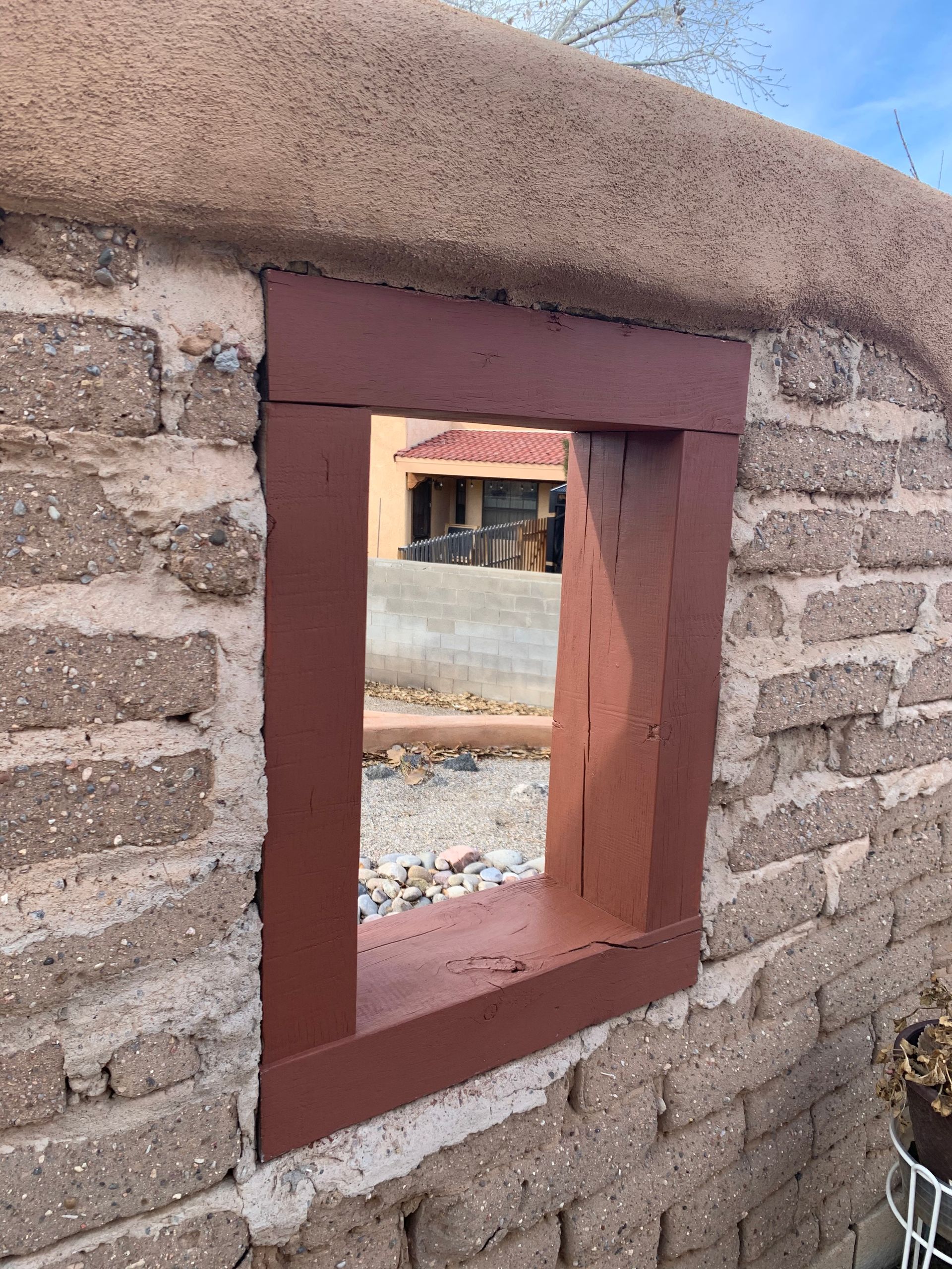 Small rectangular window opening in a stone wall with a reddish-brown frame.