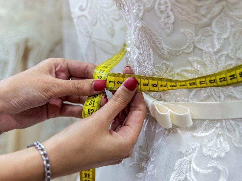 A woman is measuring the waist of a wedding dress with a tape measure.
