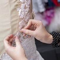 A woman is sewing a wedding dress on a mannequin.