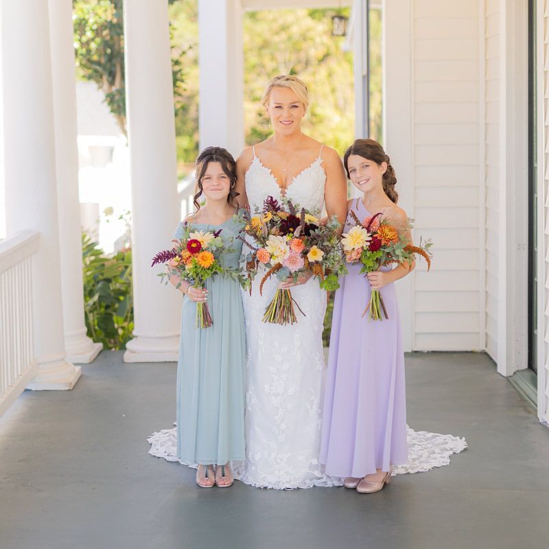 A bride and her two bridesmaids are posing for a picture on a porch.