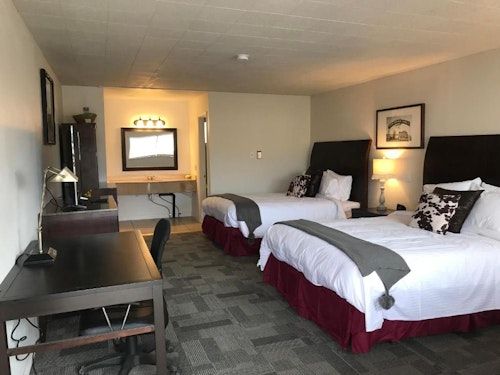 A hotel room with two queen beds, a desk, and a separate vanity area featuring a mirror, wood furniture, and grey carpet.