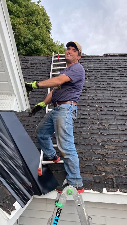 Worker in red cap and blue shirt using a drill to repair roof shingles.