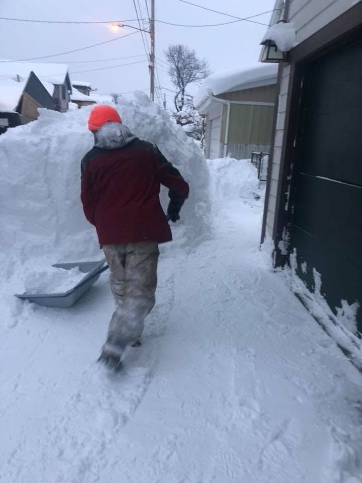 Person clearing deep snow with a snow blower beside a house