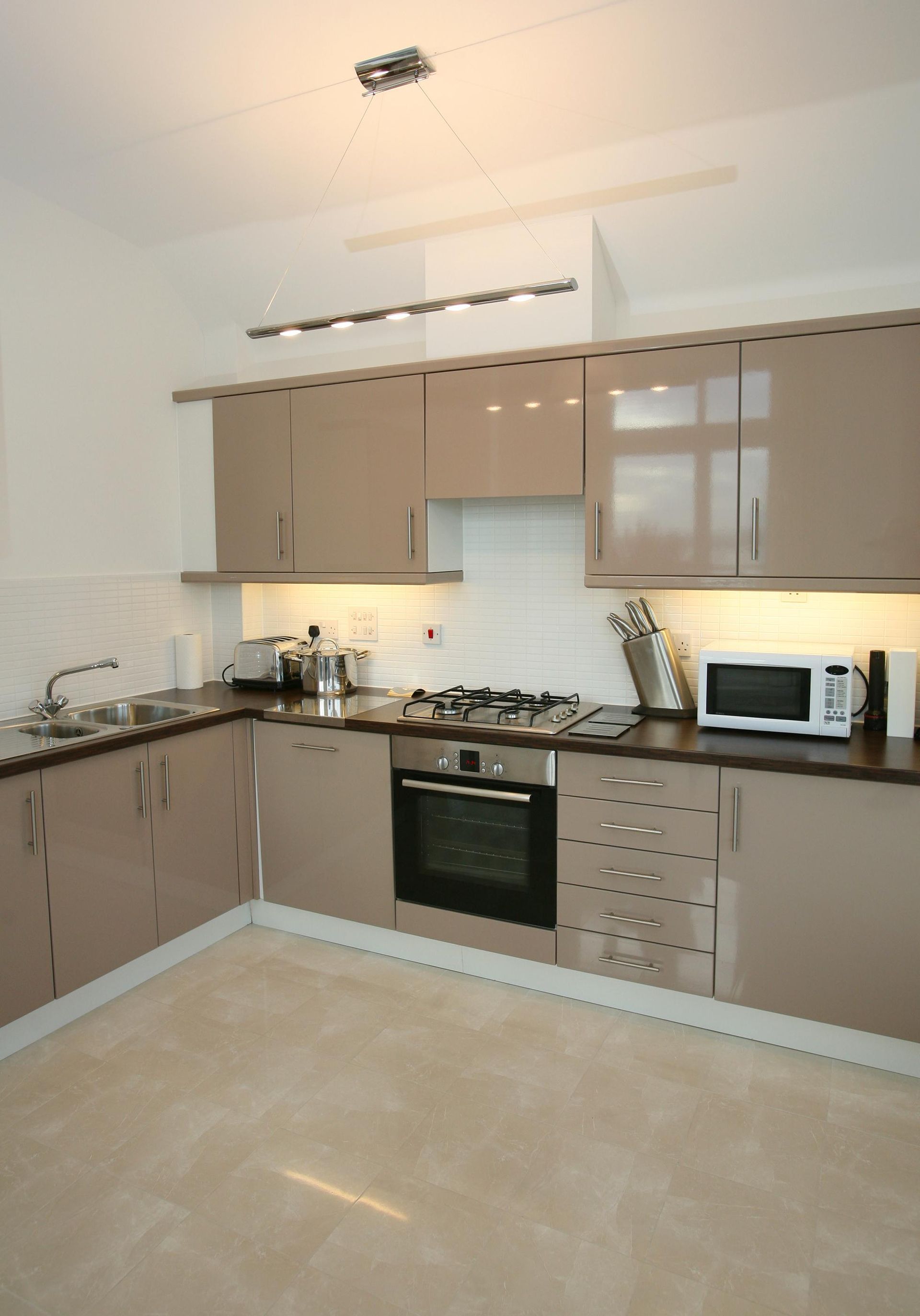 Modern beige kitchen with glossy cabinets, black countertops, built-in oven, microwave, and light tiled floor