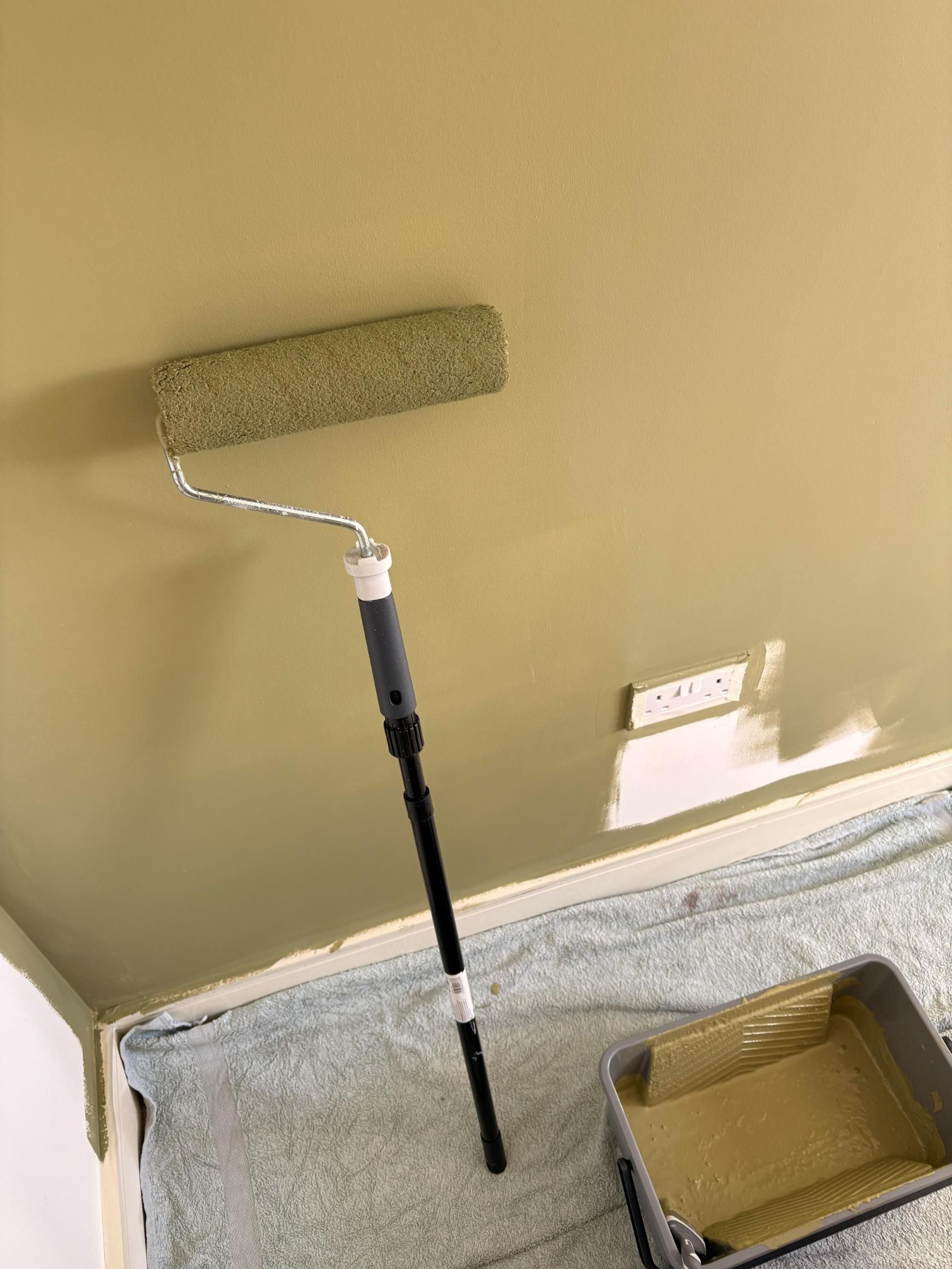 Paint roller and tray beside a tan wall in a room being painted.
