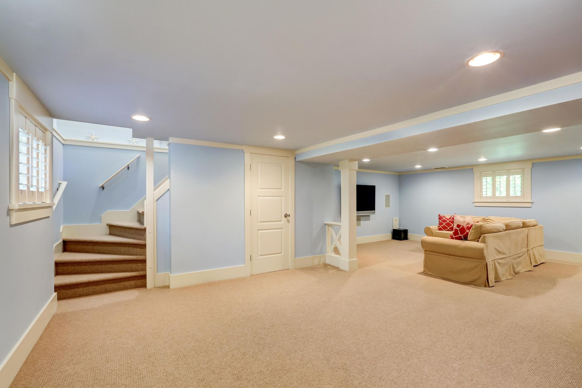 Spacious finished basement with beige carpet, light blue walls, stairs, and a sectional sofa near small windows
