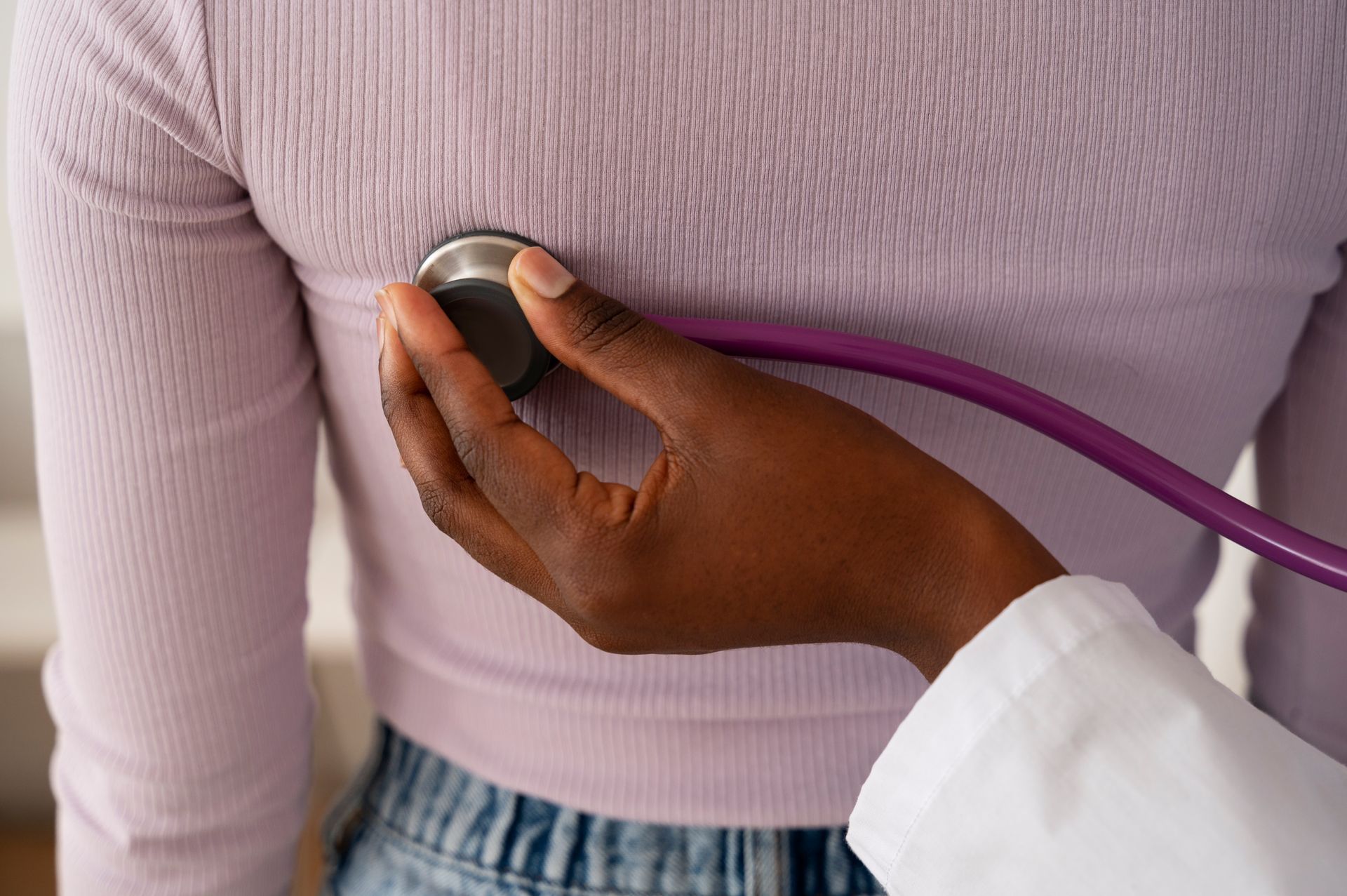 A doctor is listening to a woman 's chest with a stethoscope.