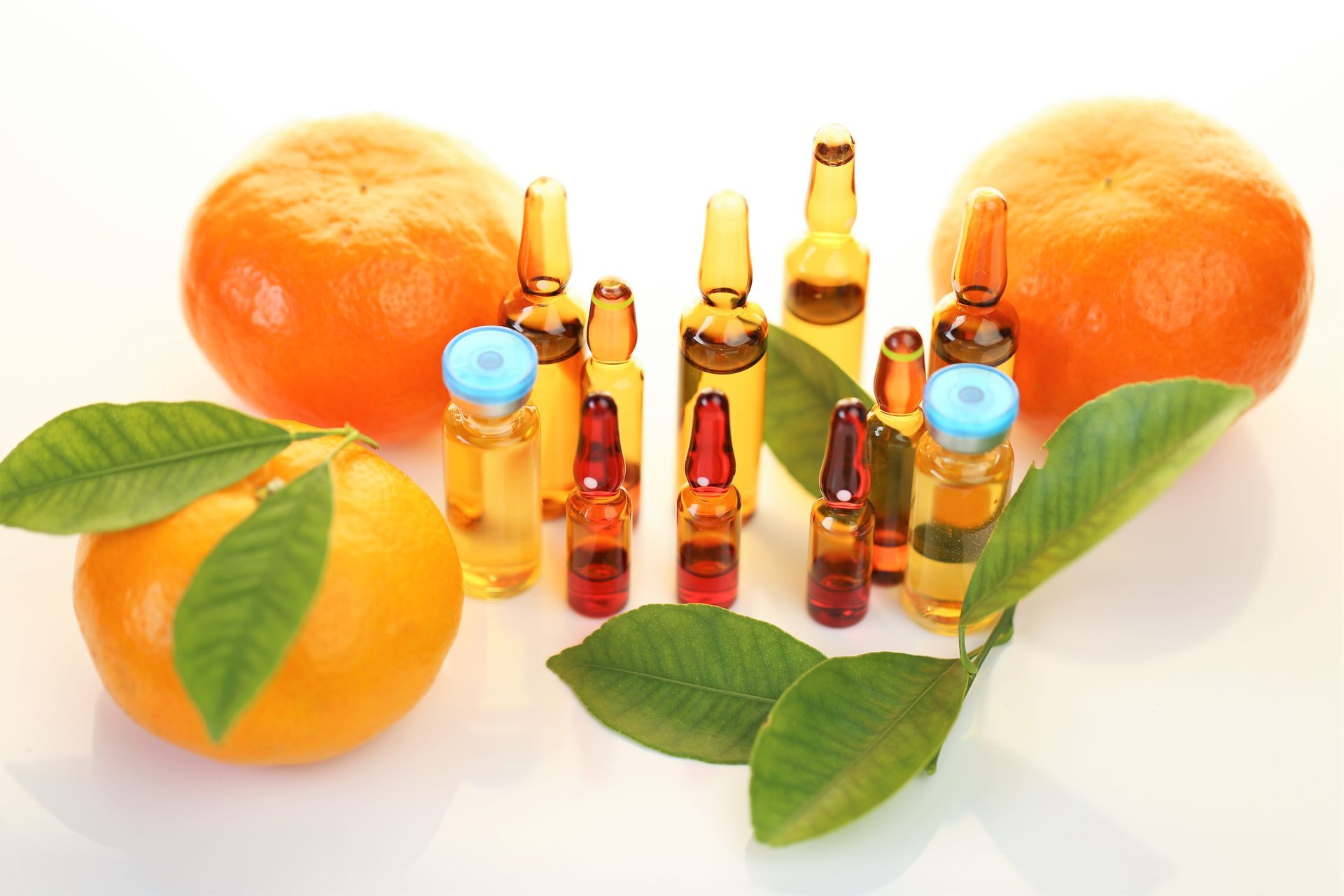 A bunch of bottles of liquid next to oranges and leaves