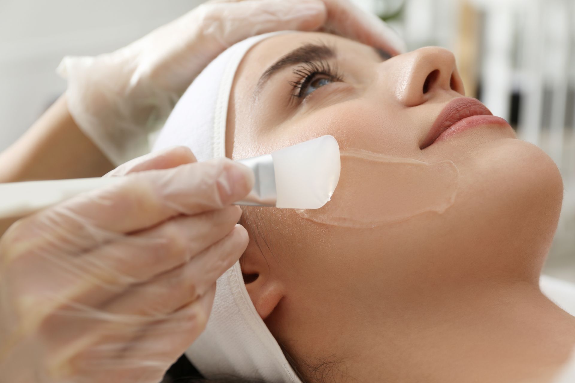 Aesthetic facial treatment being applied with a brush to a reclining woman's cheek