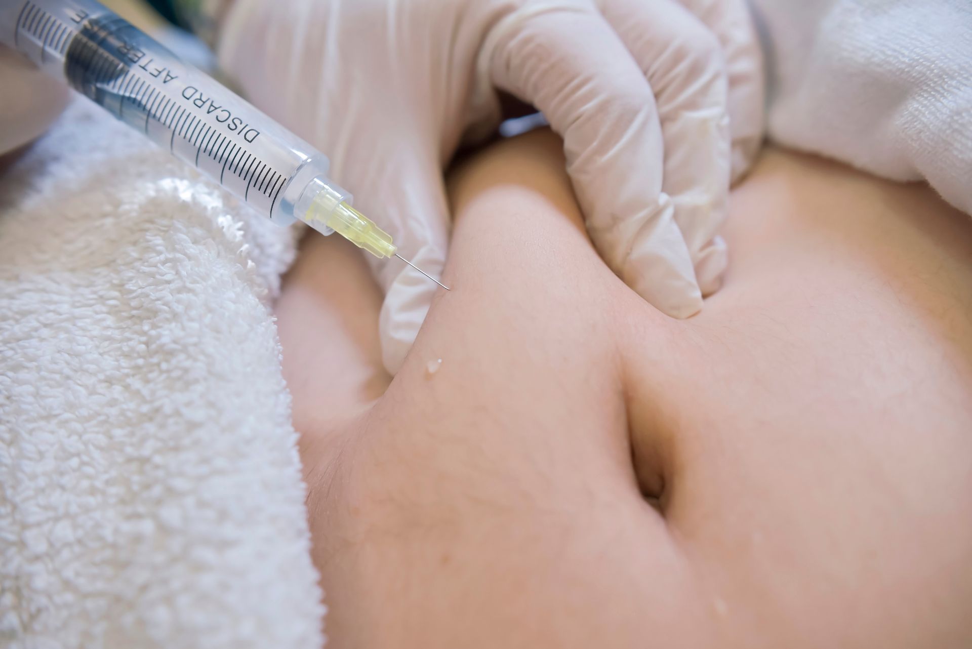 Gloved hand gives a syringe injection into an abdomen near the navel