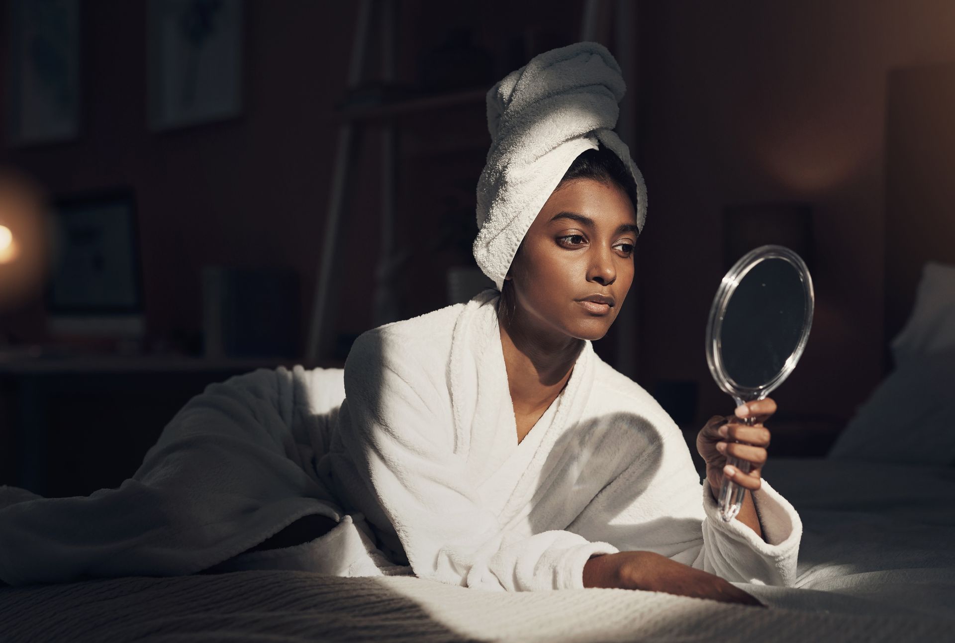 A woman with a towel wrapped around her head is looking at herself in a mirror.