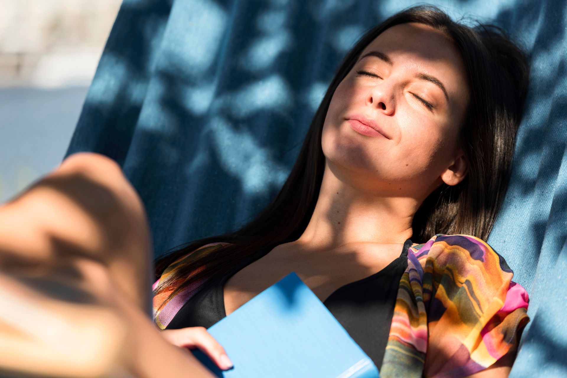 A woman is laying in a hammock reading a book.
