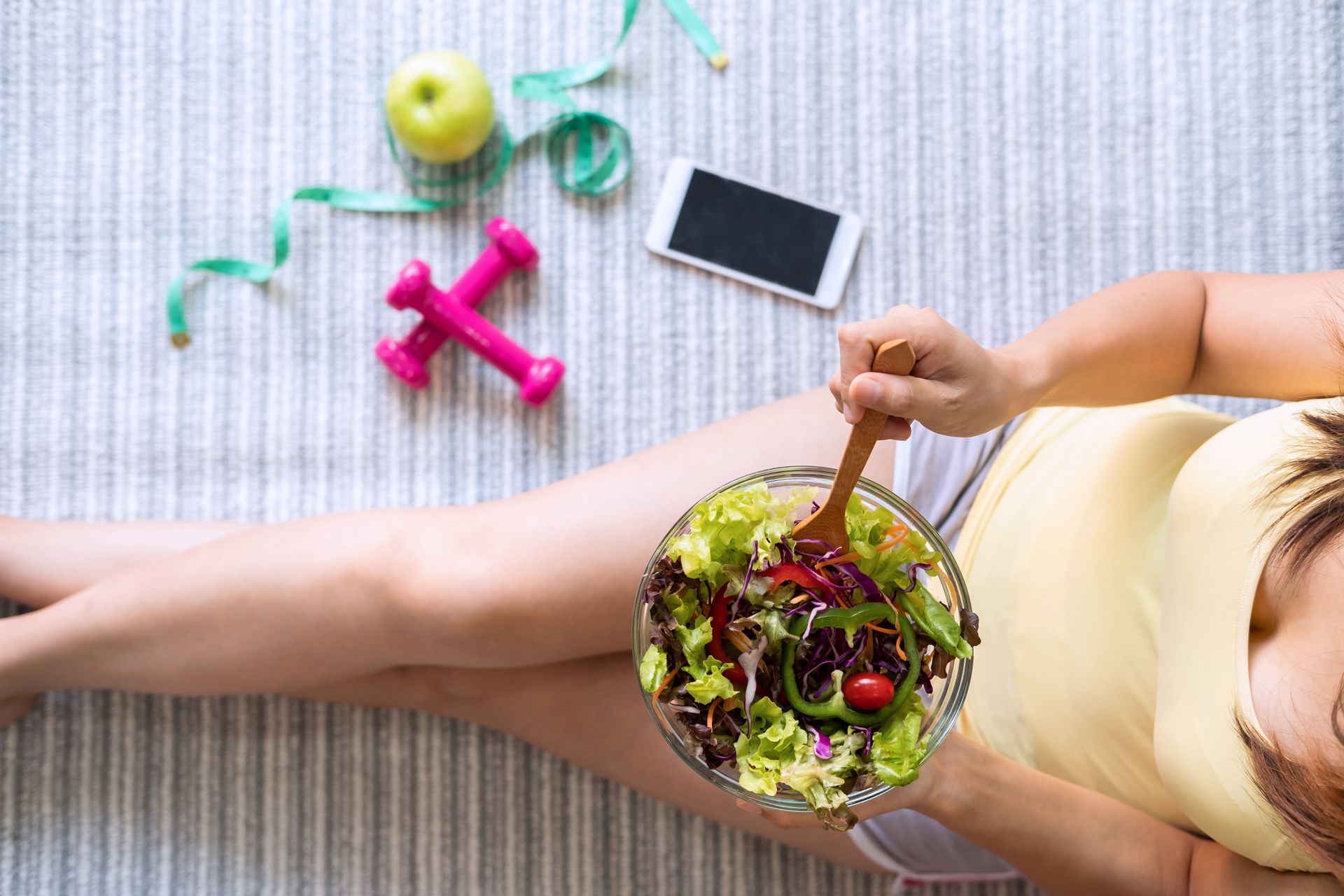 A woman is laying on the floor eating a salad.