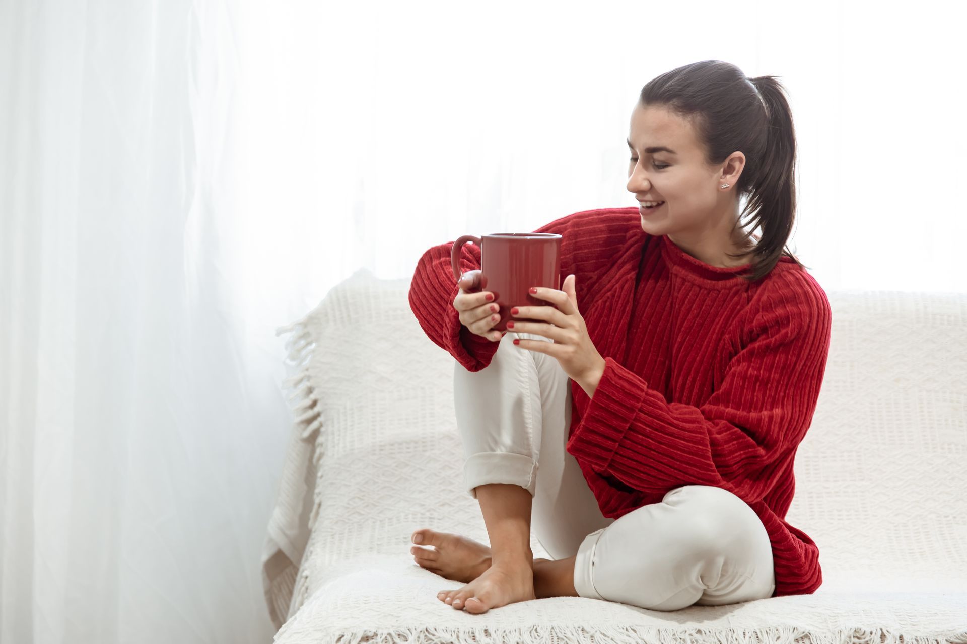 A woman is sitting on a couch holding a cup of coffee.