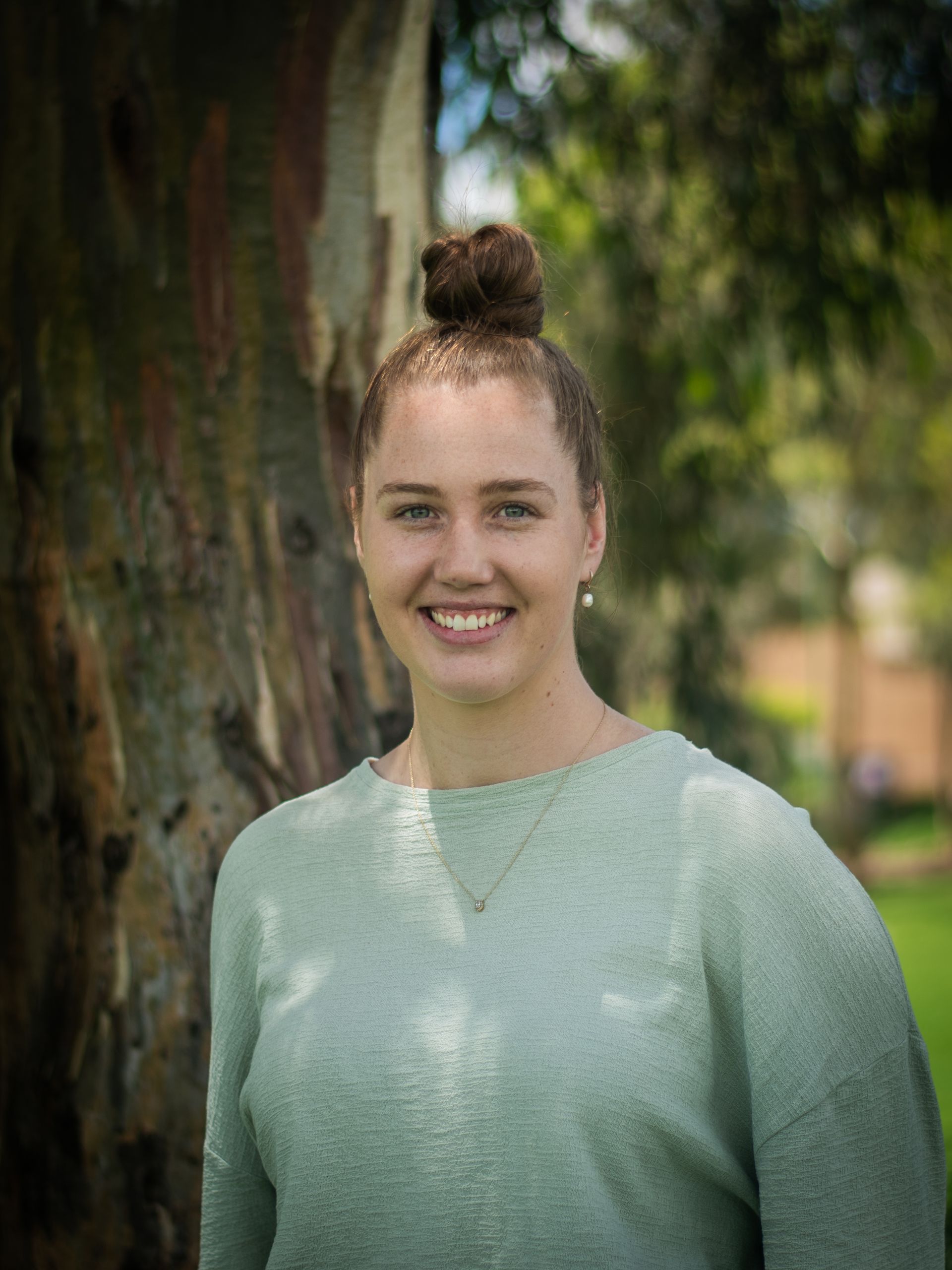 A woman in a green sweater is smiling in front of a tree.
