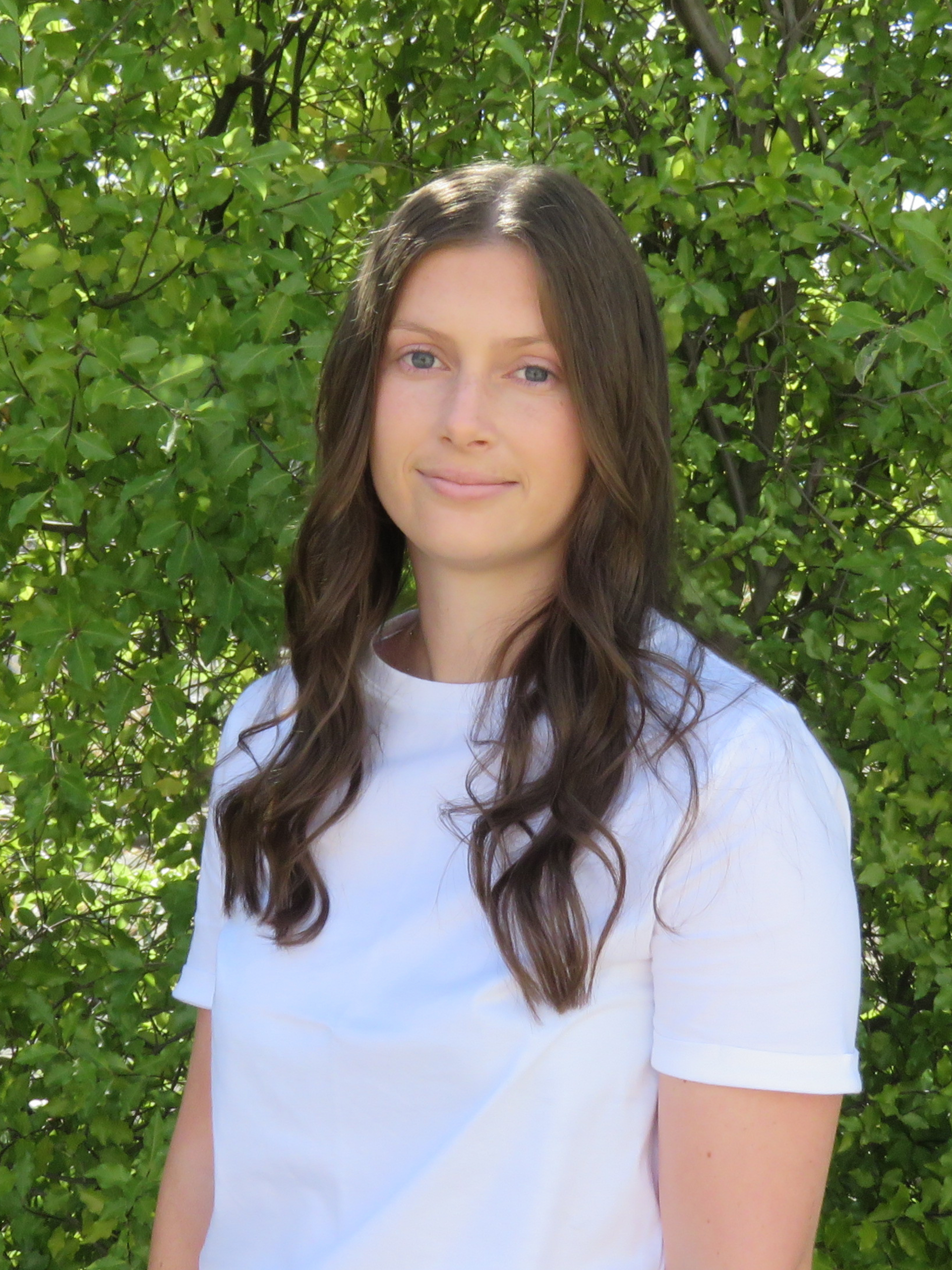 A woman in a white shirt is standing in front of a bush.