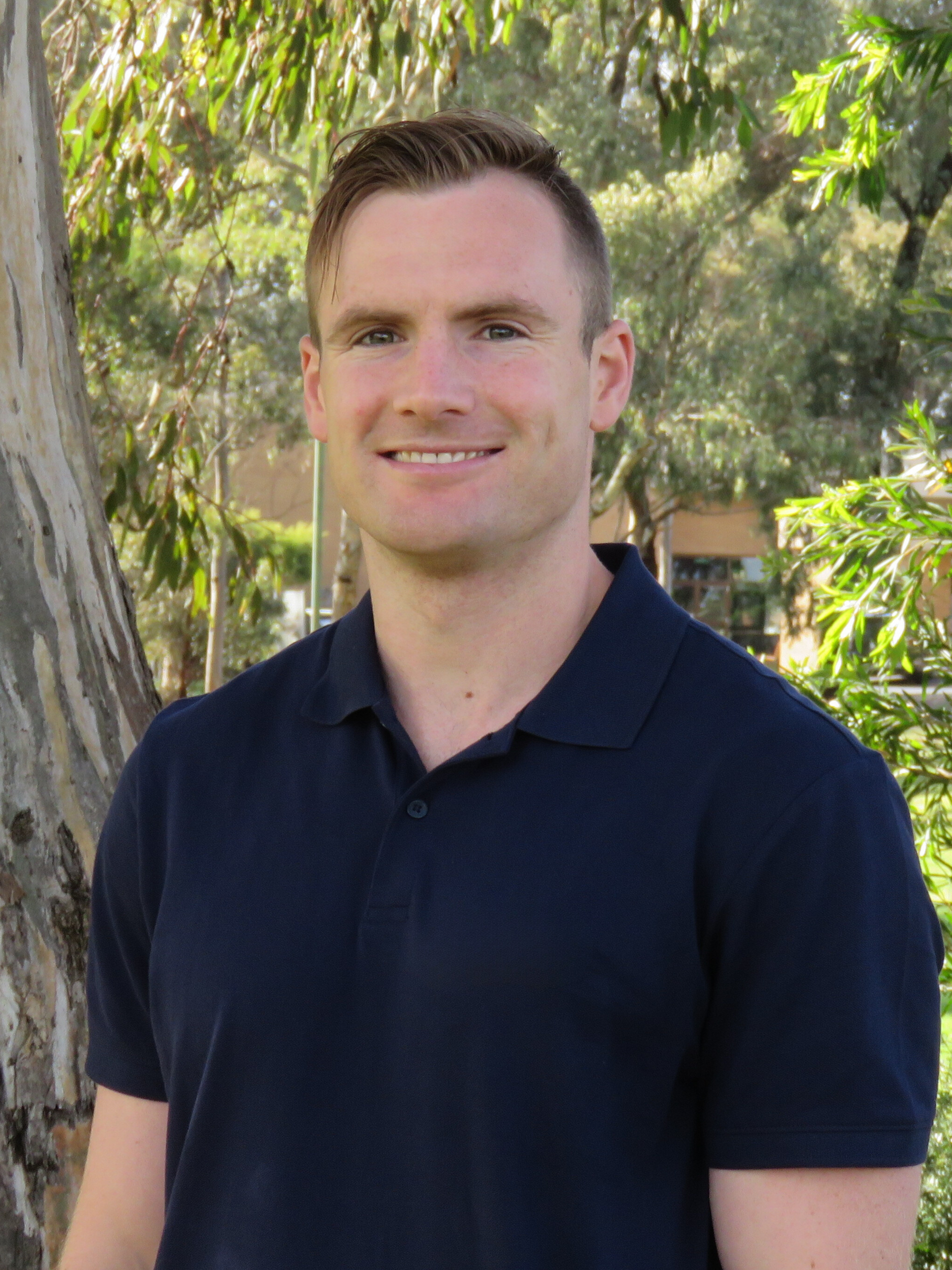 A man in a blue shirt is standing in front of a tree.
