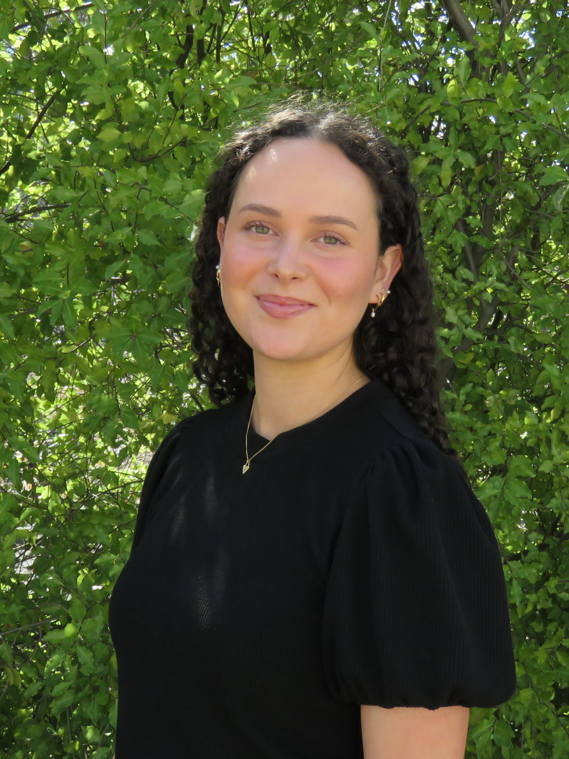 A woman in a black shirt is standing in front of a tree.