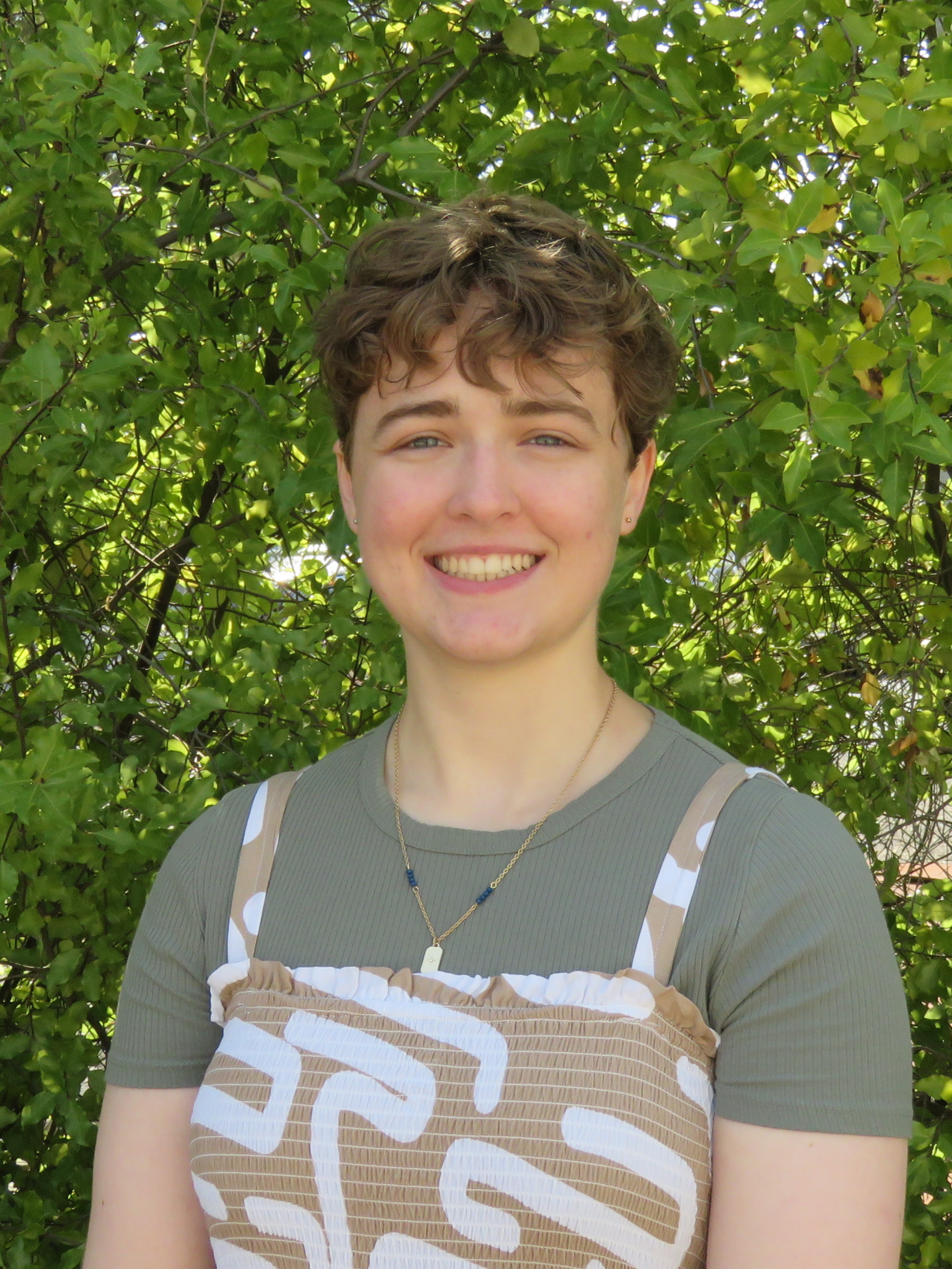 A young woman is smiling for the camera in front of a tree.