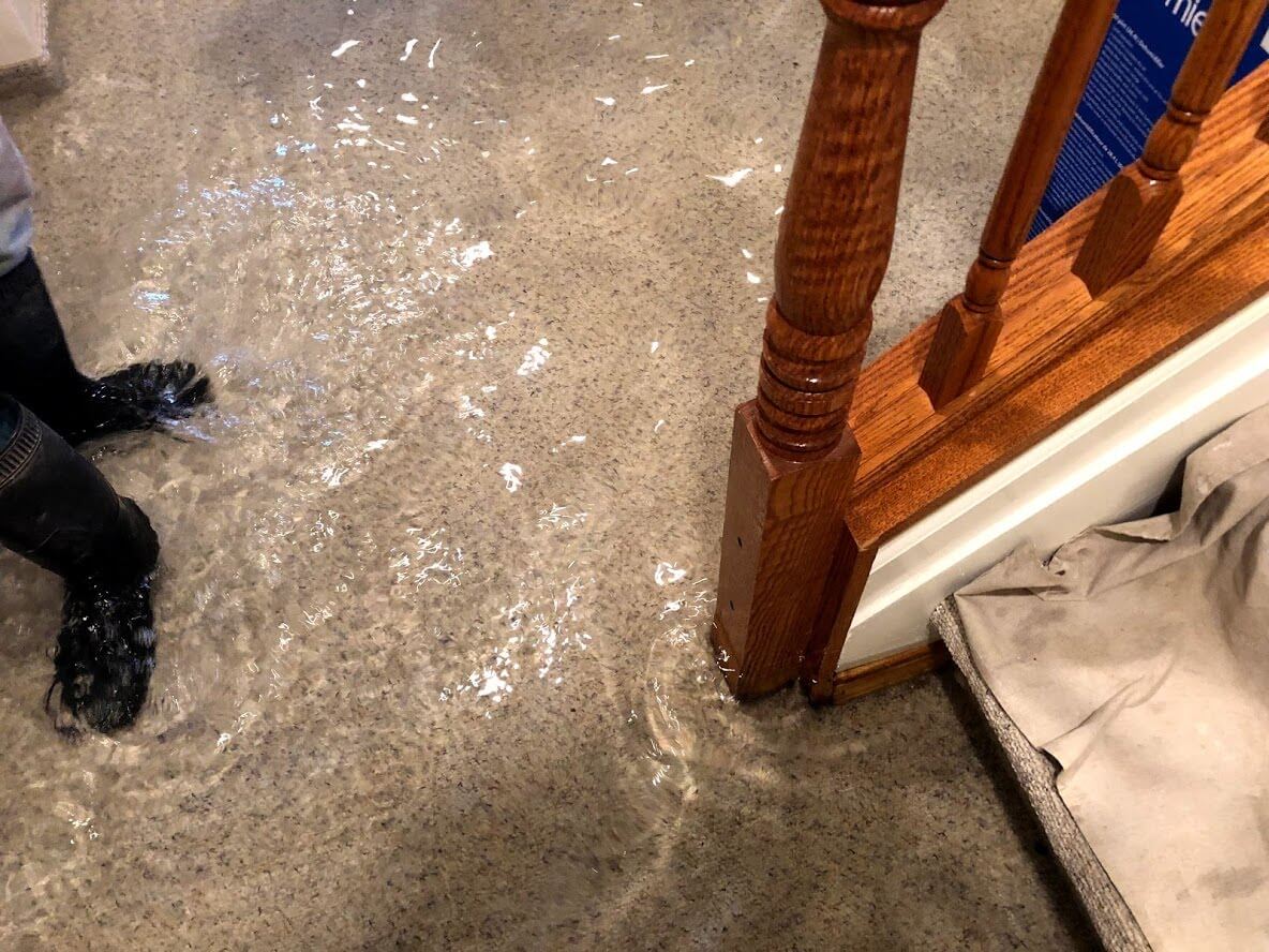 A person is standing on a flooded floor next to stairs.