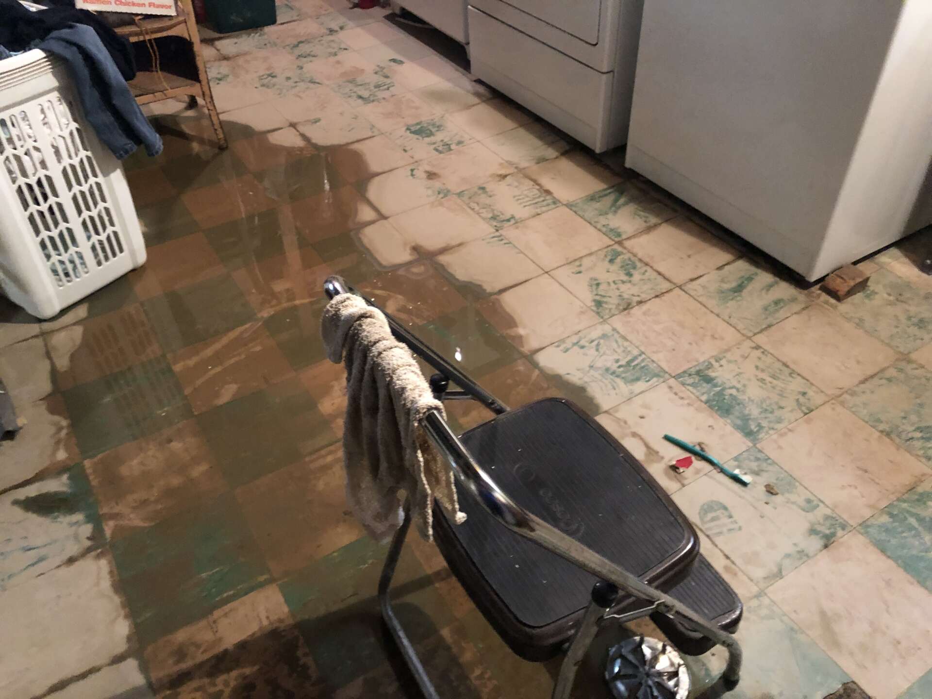 A chair is sitting in a flooded laundry room next to a washer and dryer.