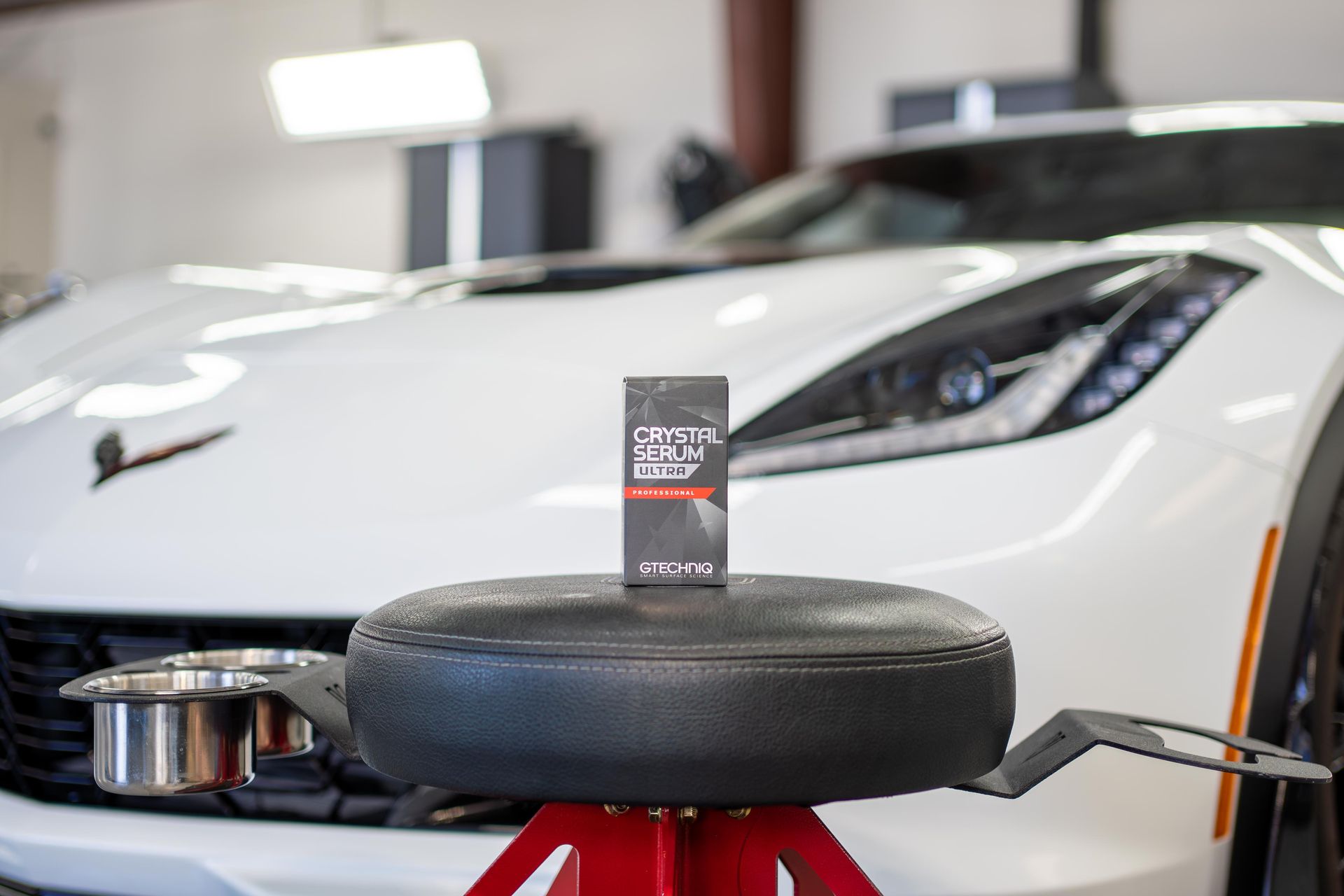 Car detailing setup with a white sports car, polishing pad, and product on a red stand