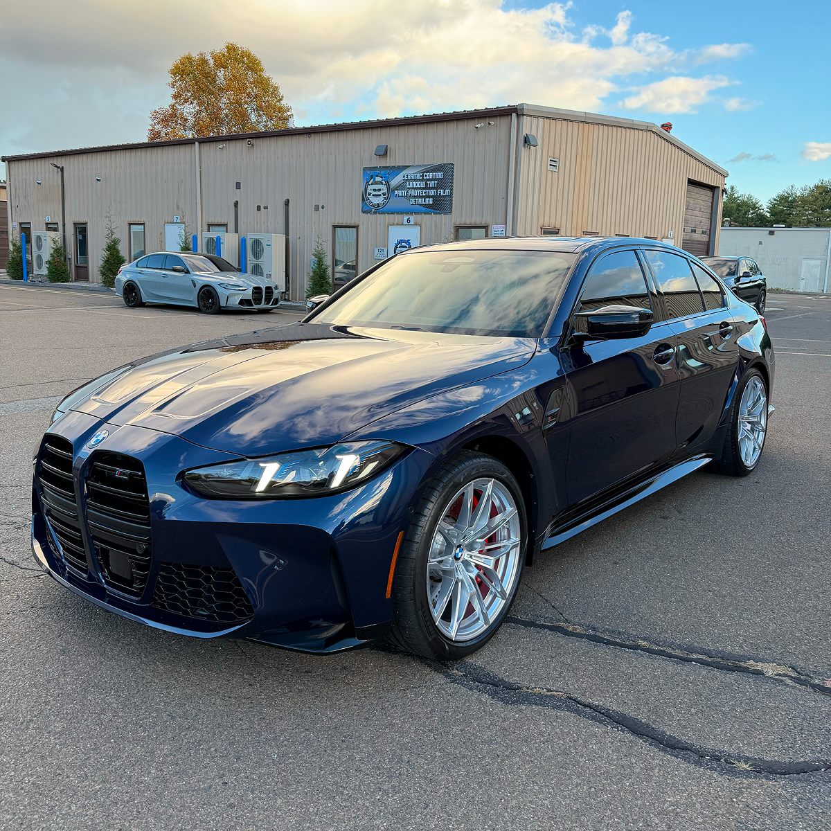 Dark blue BMW sedan parked outside an industrial building at sunset