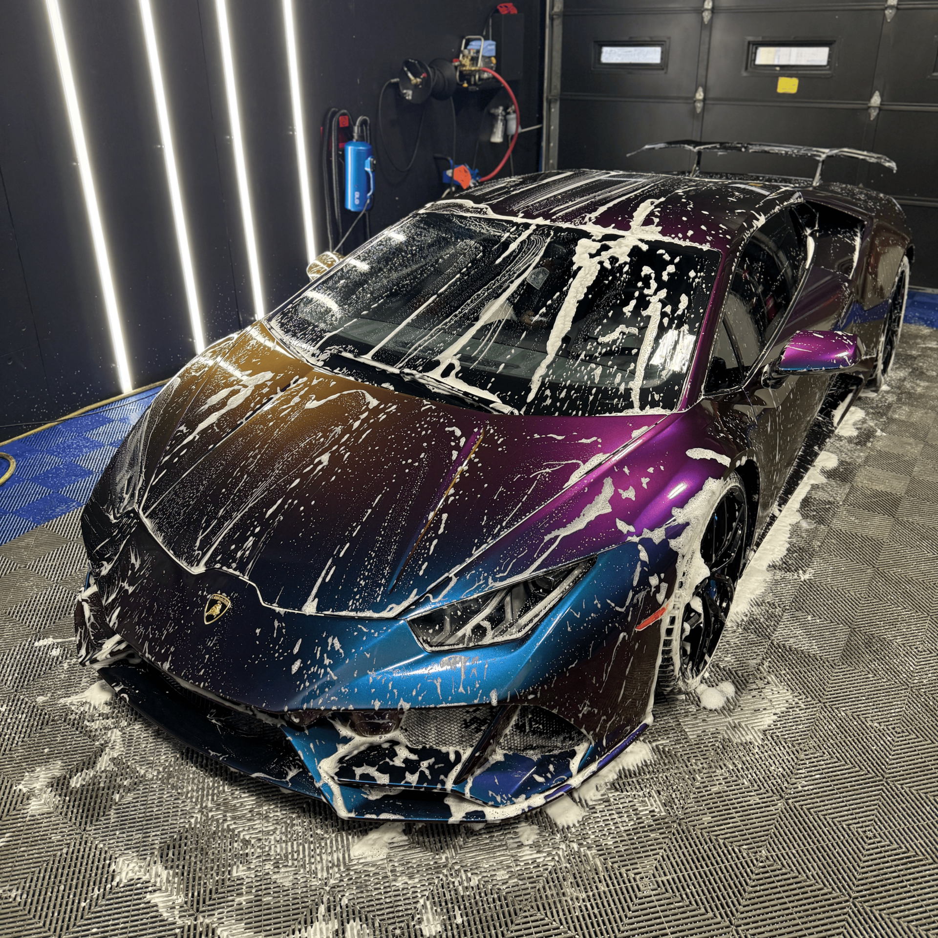 Purple-blue sports car covered in foam inside a car wash bay