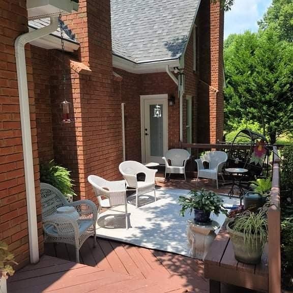 Outdoor patio with white chairs, rug, and potted plants next to a brick building.