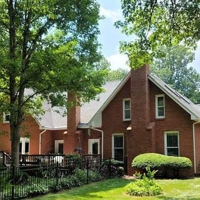 Red brick house with a chimney, windows, and lush green trees.