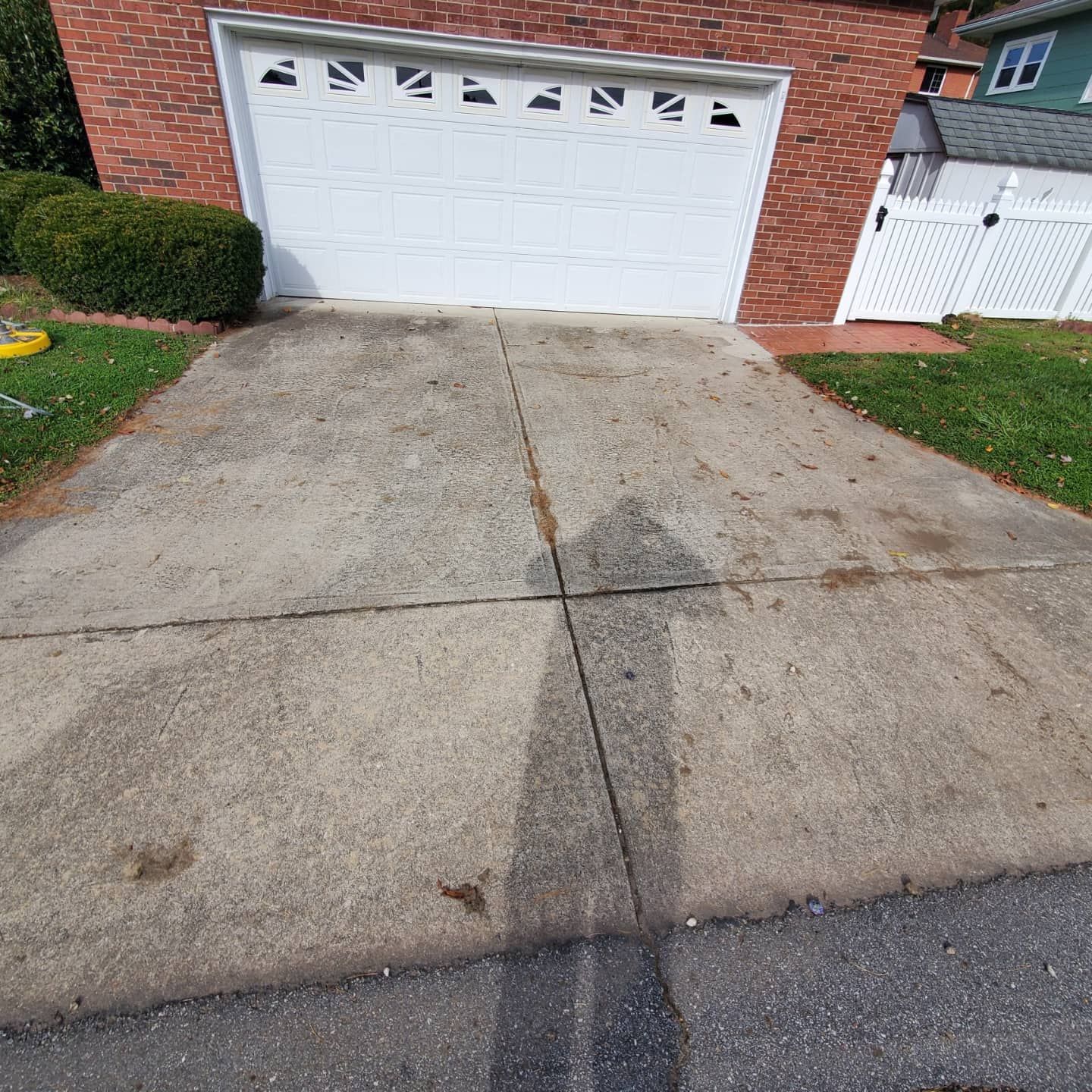 Concrete driveway leading to a white garage door, adjacent to grass, bushes, and brick wall.