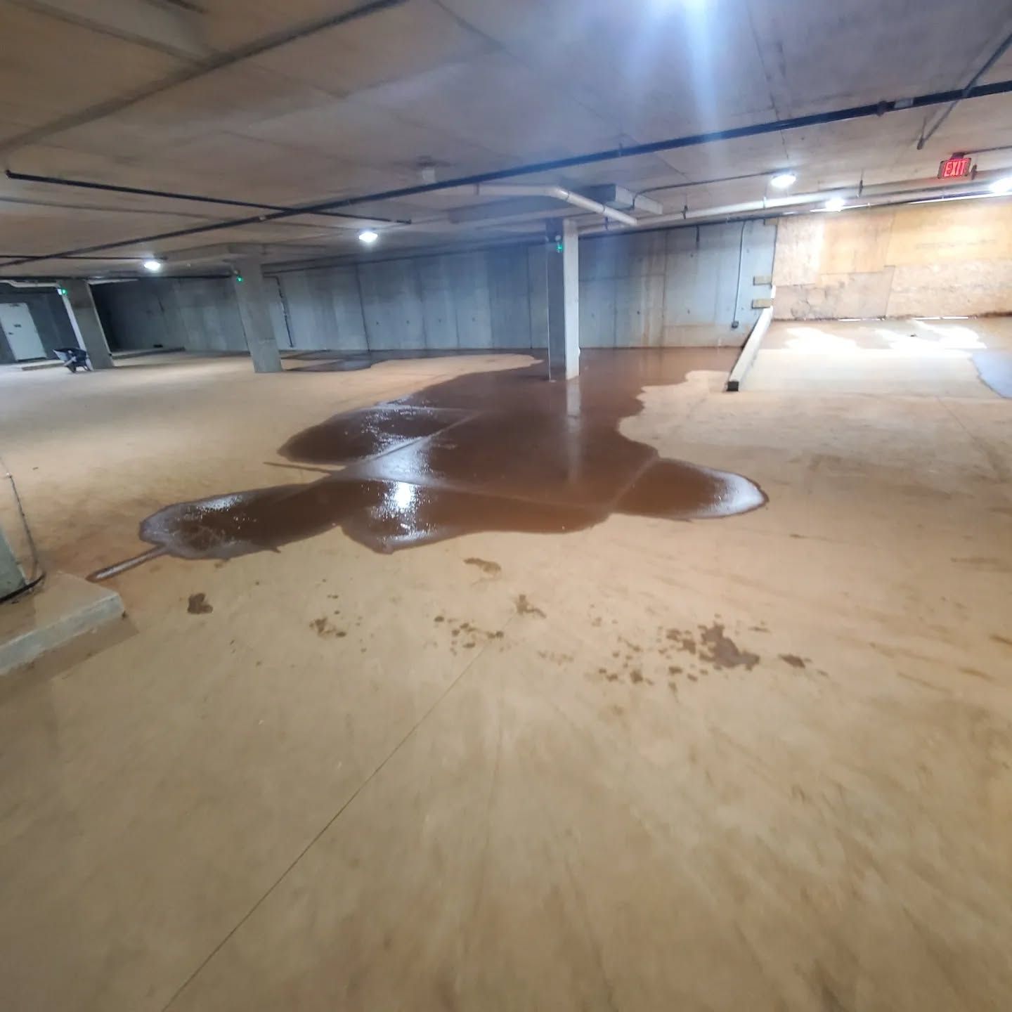 Flooded concrete basement with brown water pooling on the floor, under industrial lighting.