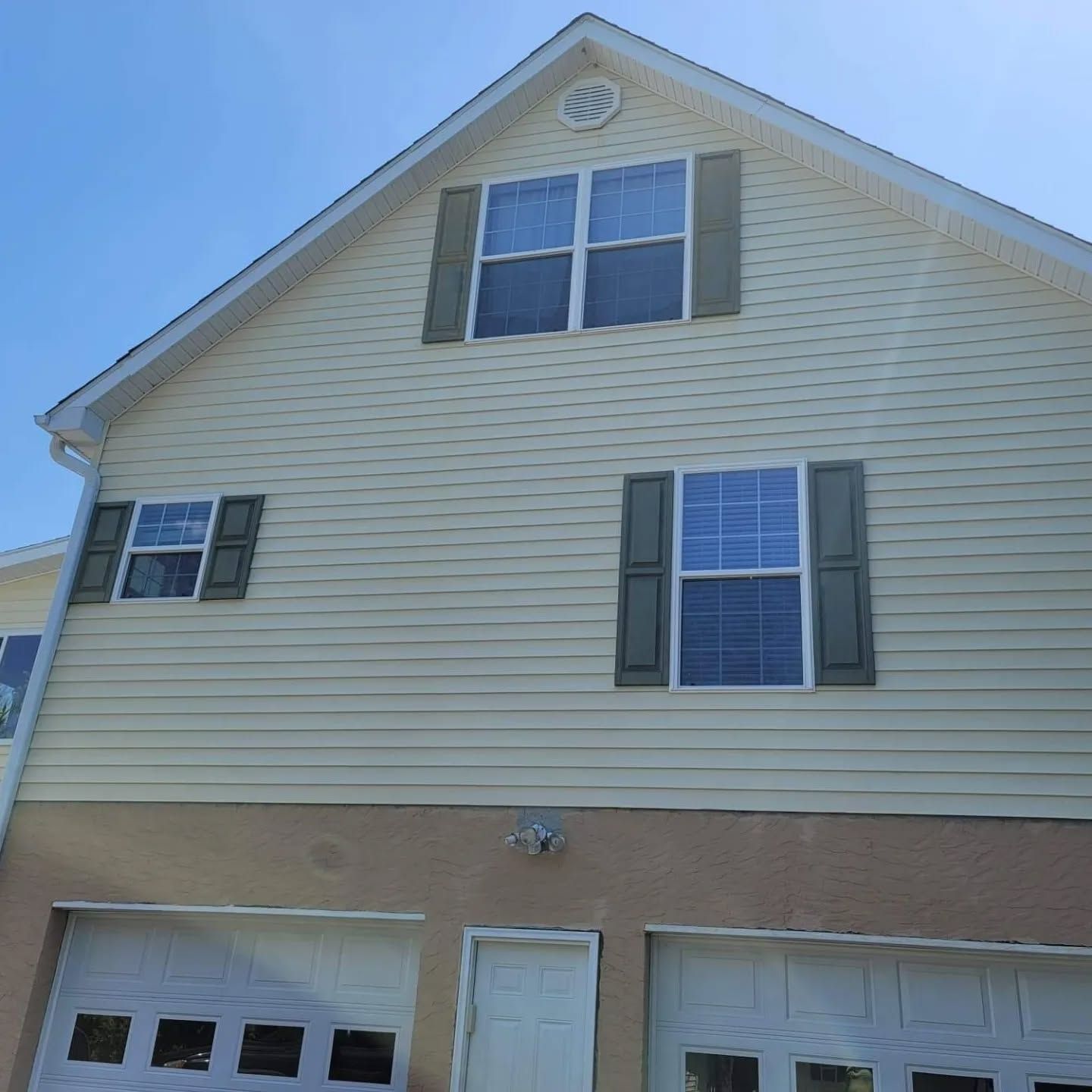 Beige house with two-car garage, multiple windows, green shutters, and blue sky.