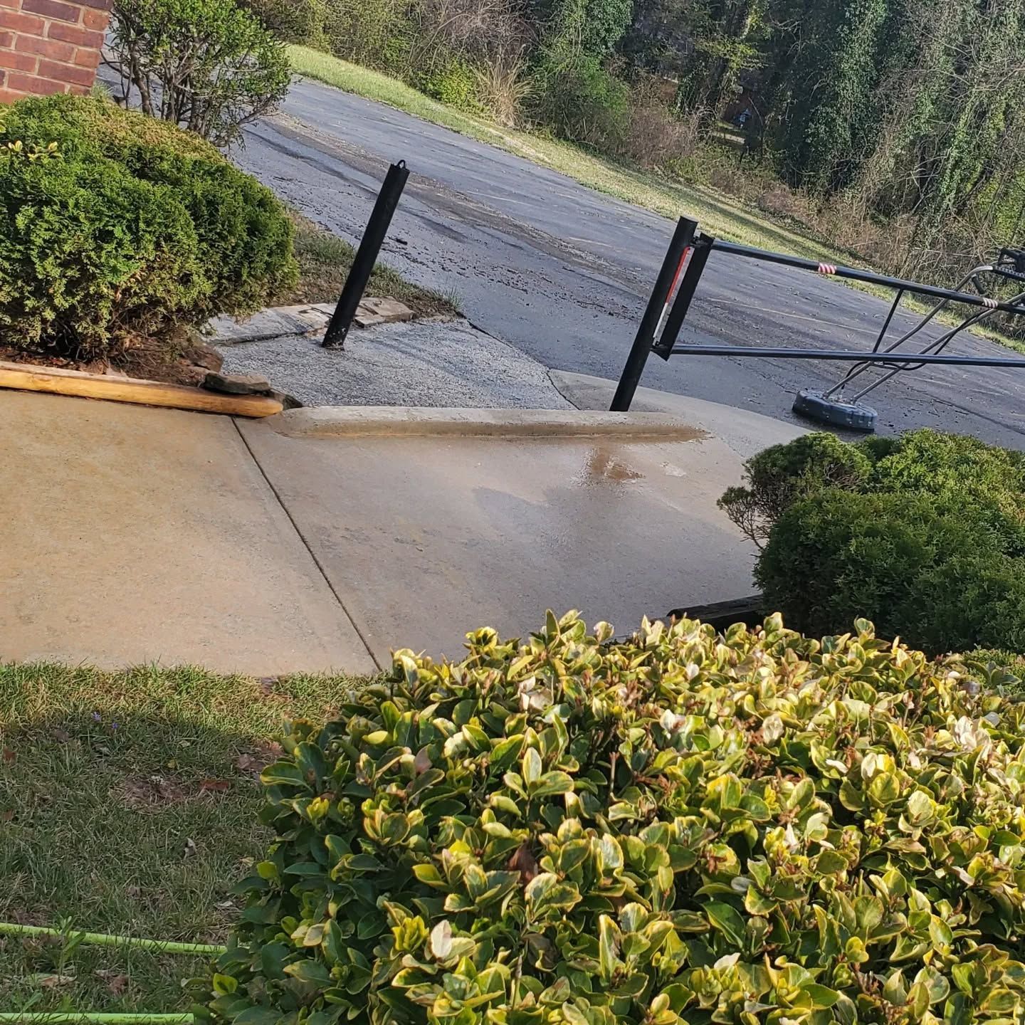 Damaged concrete driveway with fallen metal fence and wet pavement.