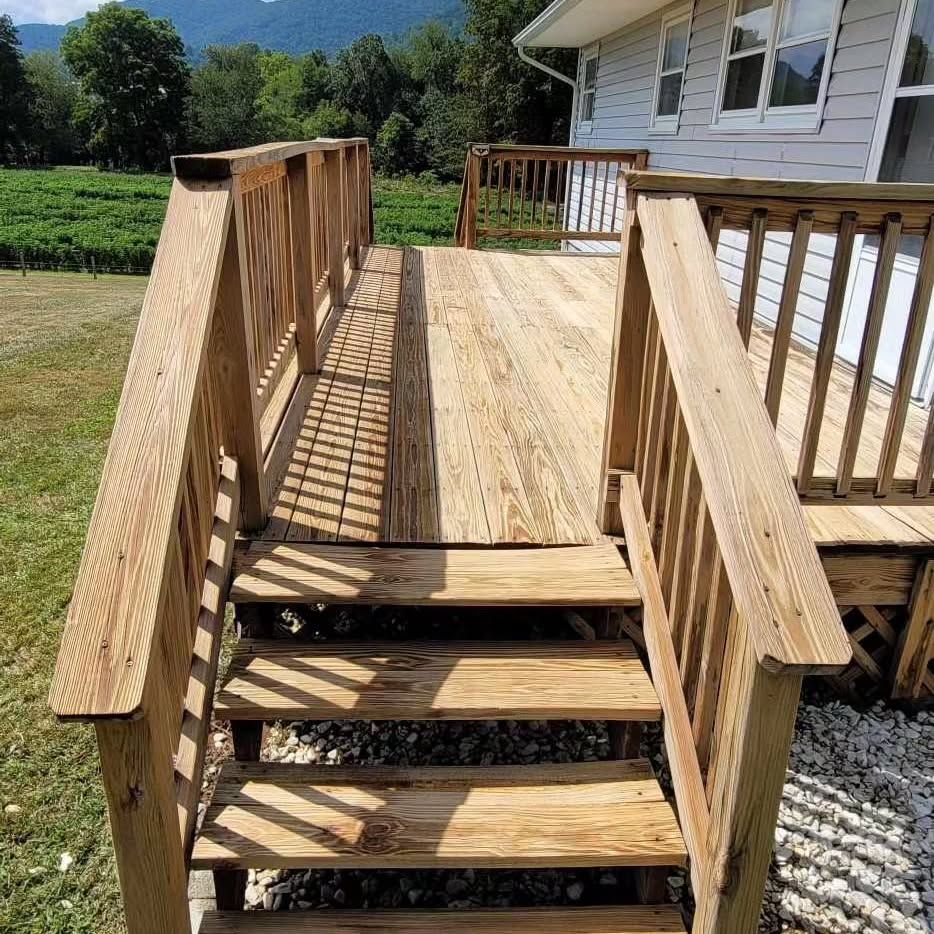 Wooden deck and stairs leading from a house, with railing and surrounding vegetation.