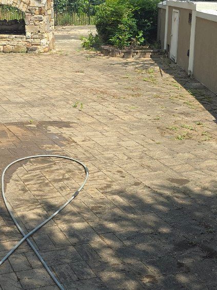 Brick patio with a hose, stone structure on the left, and a white wall with doors on the right.