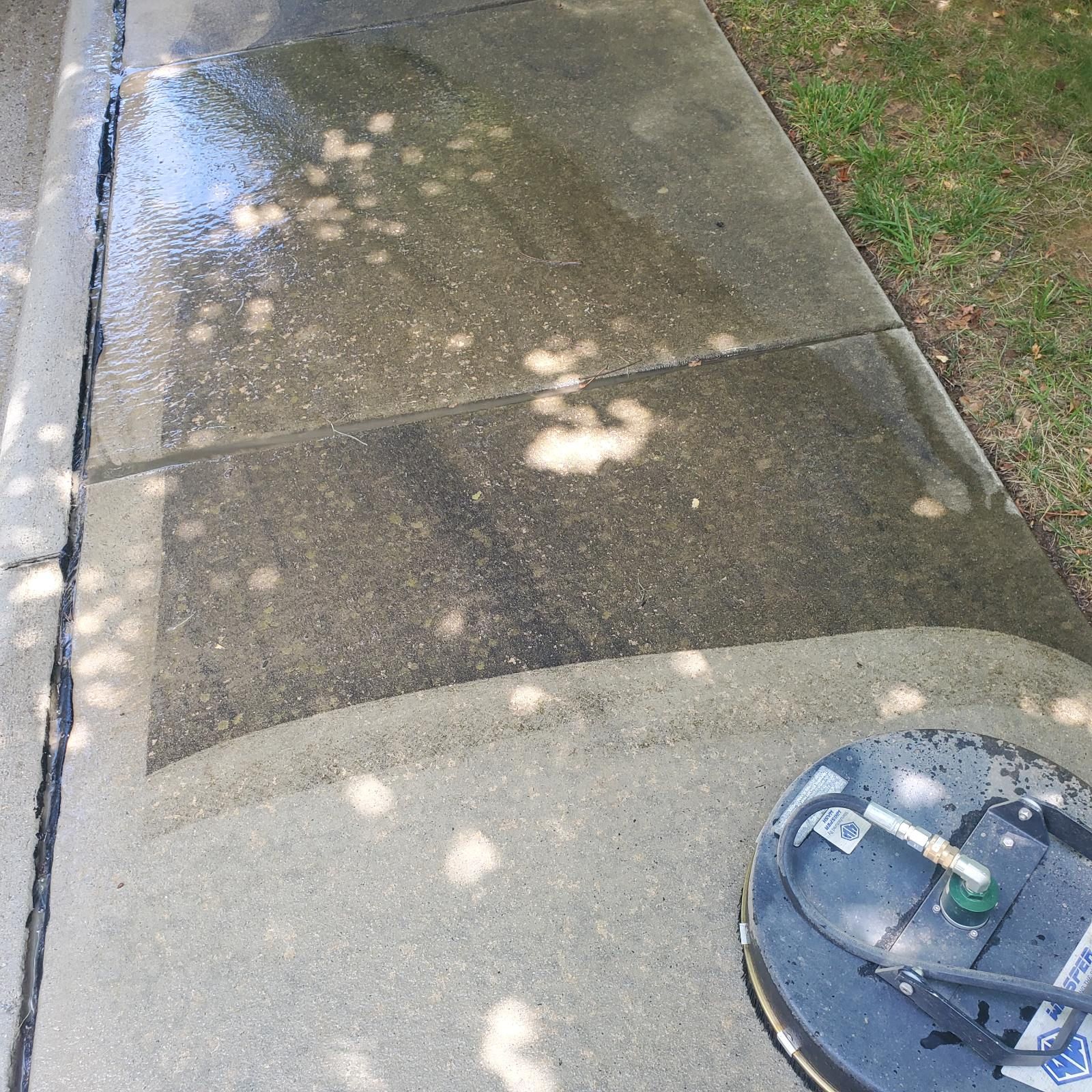 A person power washing a concrete sidewalk. The surface is wet with areas cleaned.