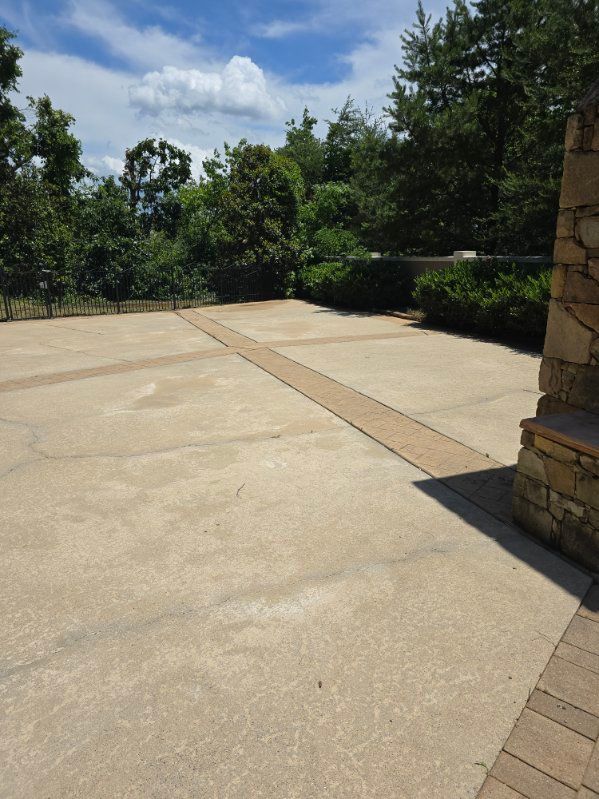 Concrete patio with stone accent strip and bordering greenery under a blue sky.