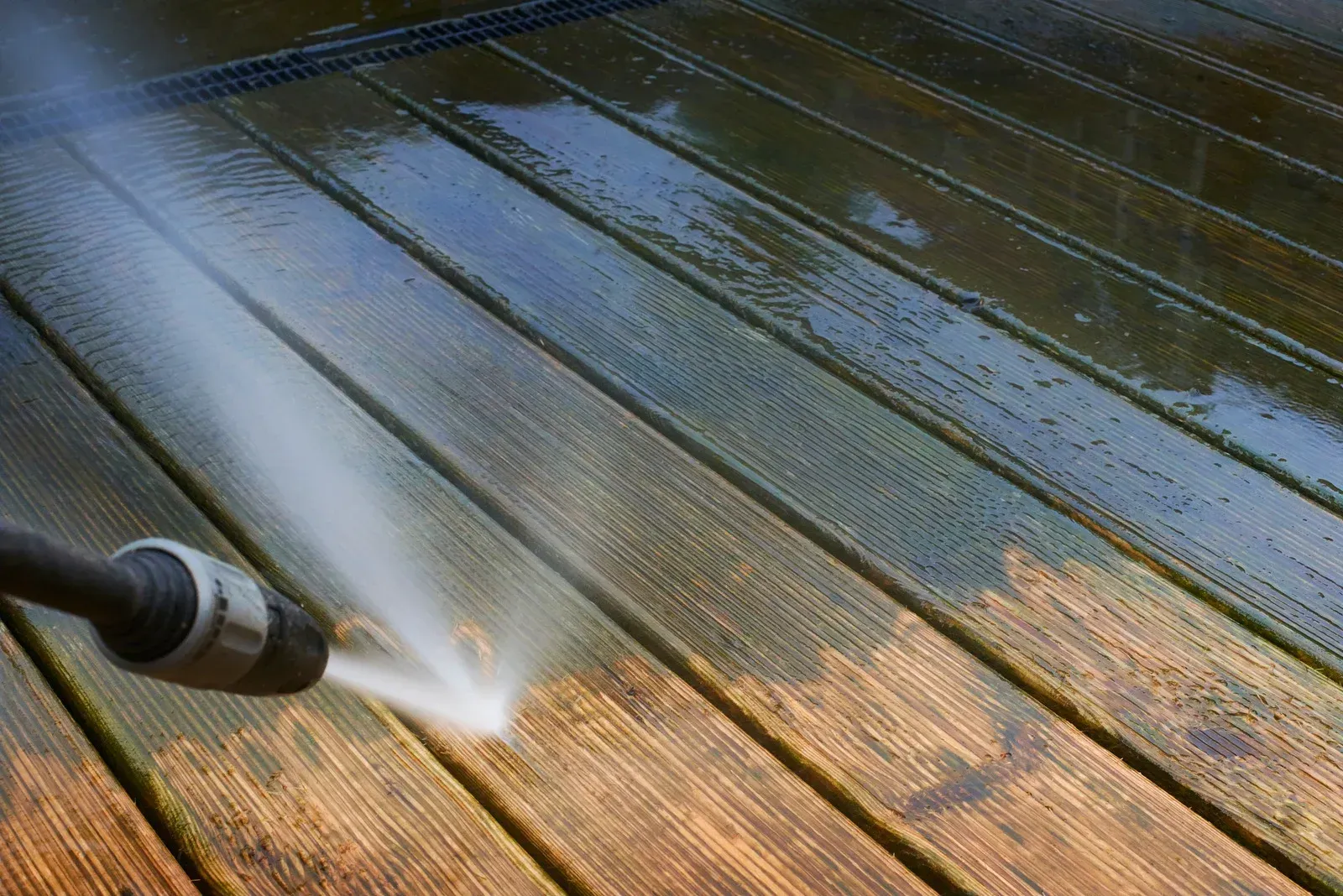 Pressure washing a wooden deck, revealing clean, wet boards.