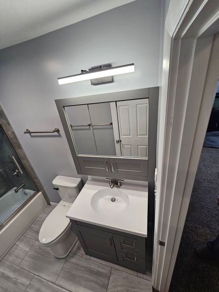 High-angle view of a bathroom with a grey vanity, white countertop, mirror, toilet, and a tiled shower on the left.