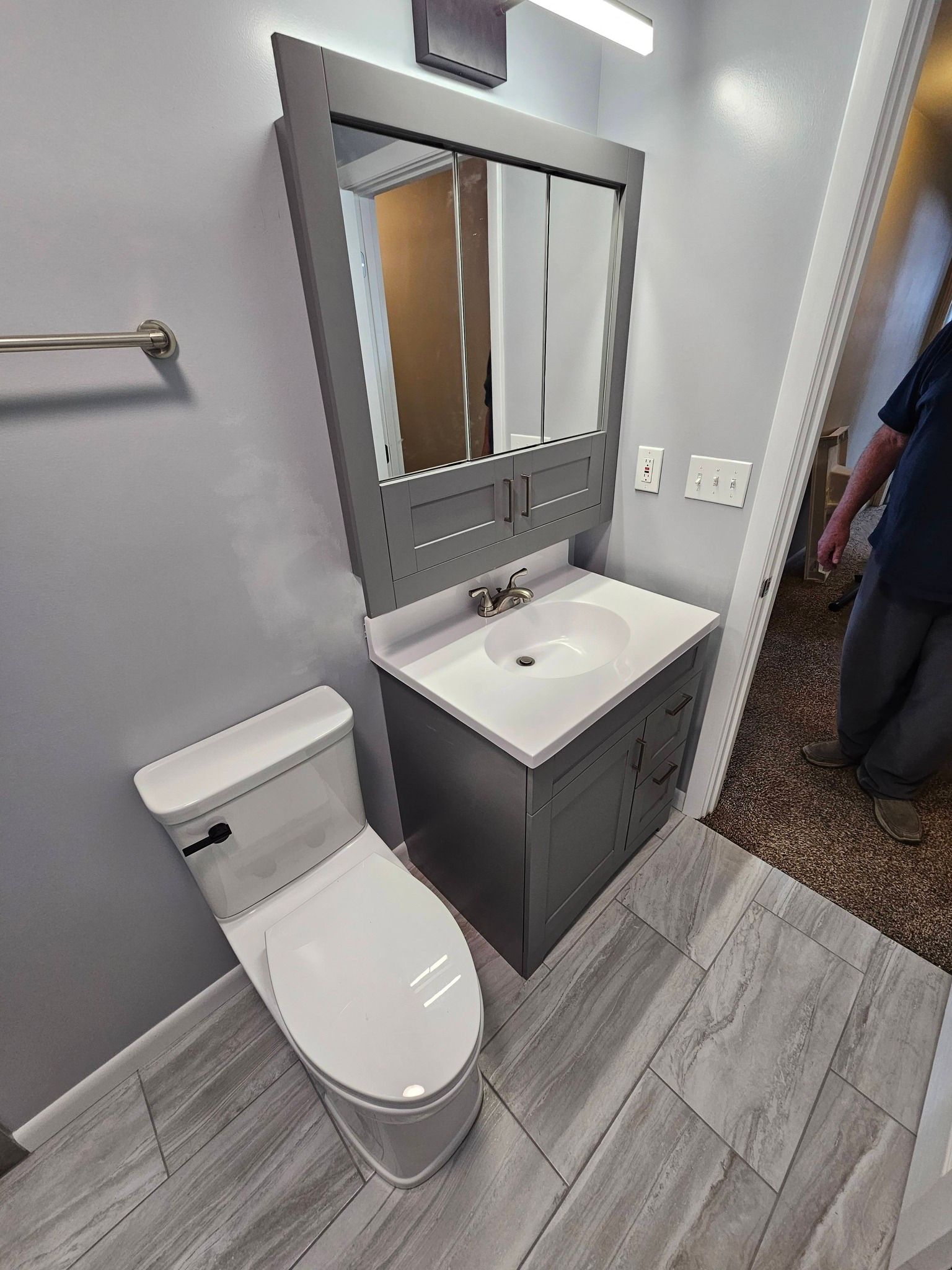 A high-angle view of a bathroom featuring a gray vanity with a white sink, a matching mirror, and a white toilet.
