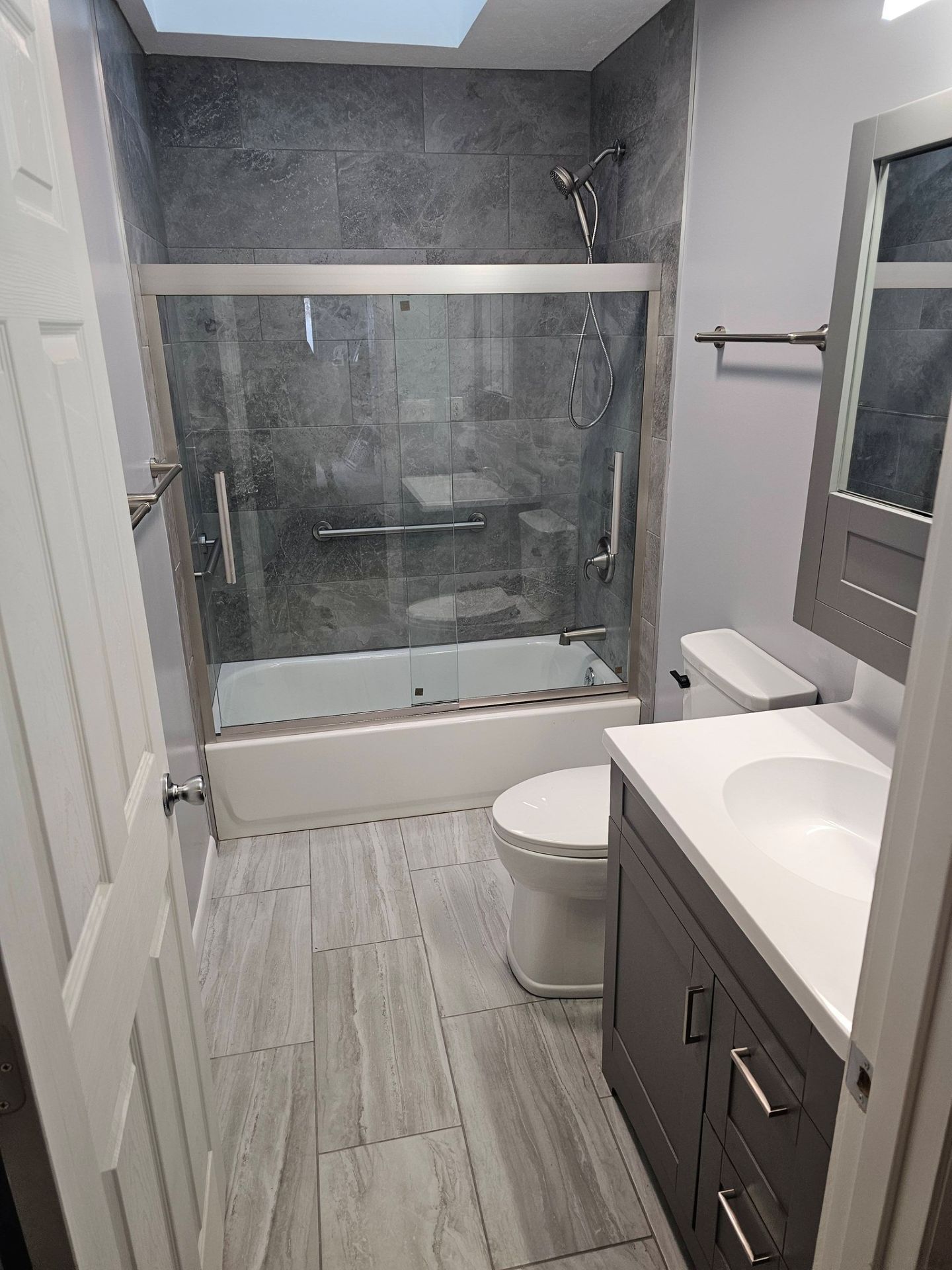 A bathroom featuring gray tile, a sliding glass door shower-tub, a white toilet, and a vanity with a white countertop.