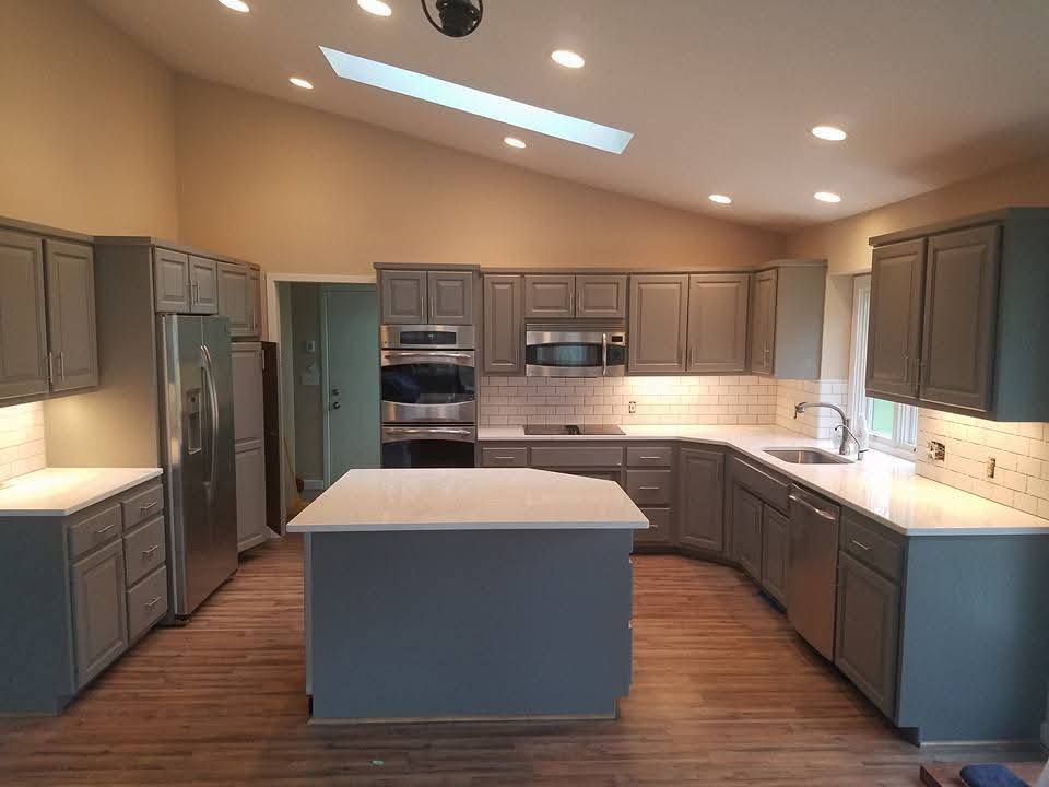 A modern kitchen with grey cabinets, white countertops, stainless steel appliances, and a central island under a skylight.