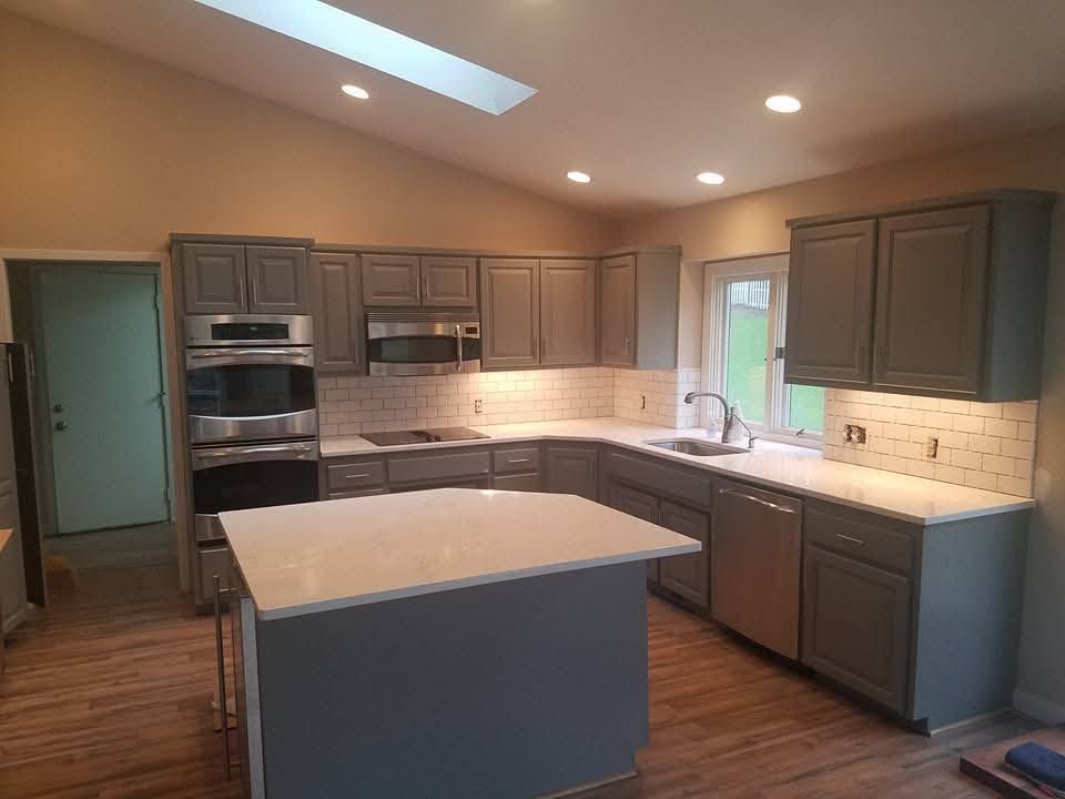 A modern kitchen featuring gray cabinets, white countertops, a center island, stainless steel appliances, and a skylight.