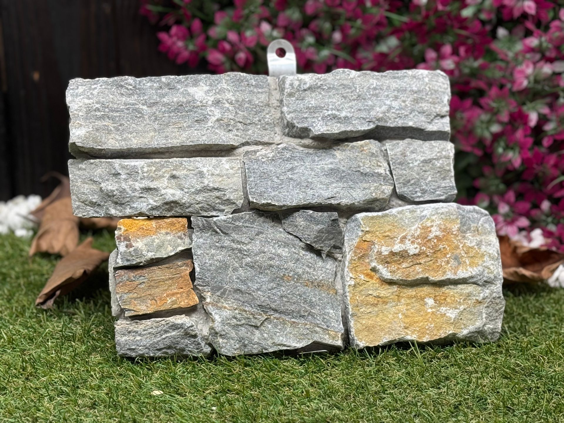 Steinblockmauer mit grauen und goldfarbenen Steinen; Metallaufhänger.