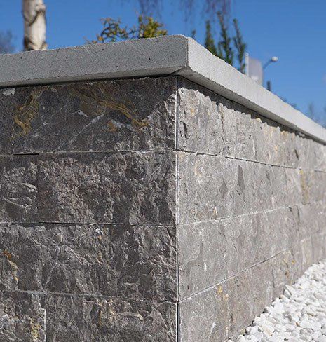 Steinmauer mit grauer Betonabdeckung vor blauem Himmel.