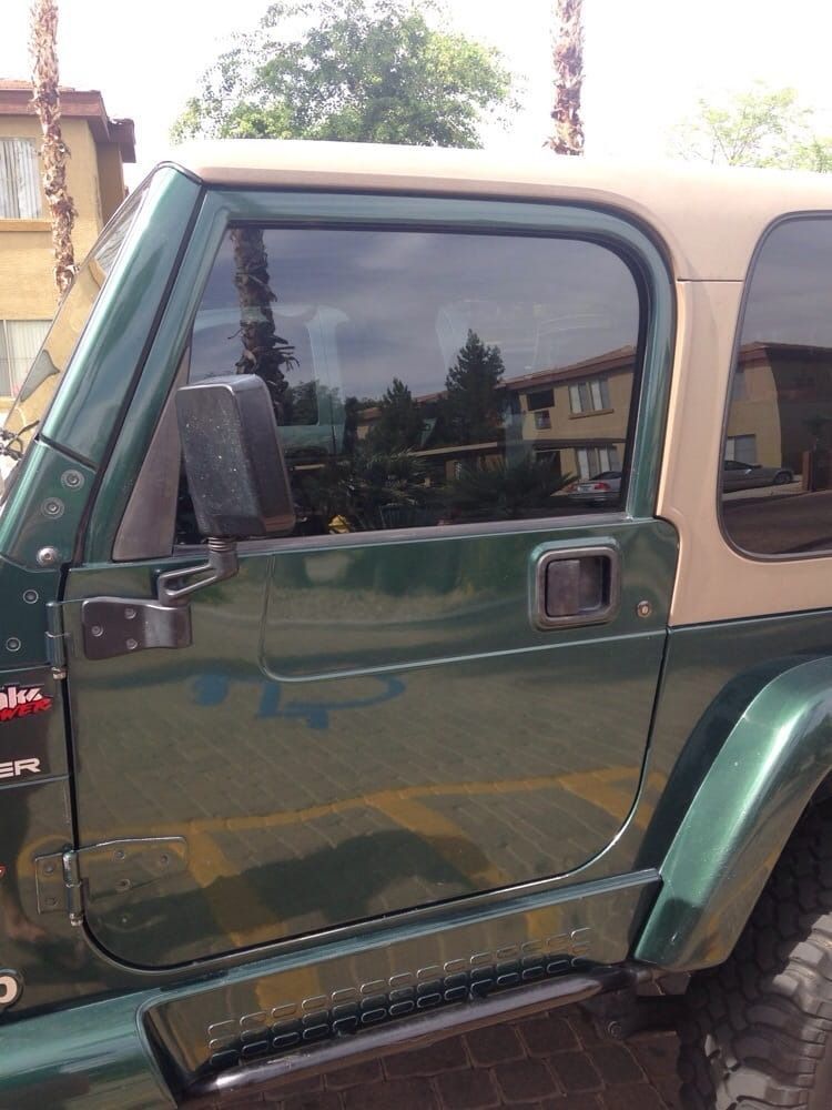 A green jeep with a tan top is parked in a parking lot.