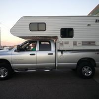 A silver truck with a camper on top of it is parked on the side of the road.